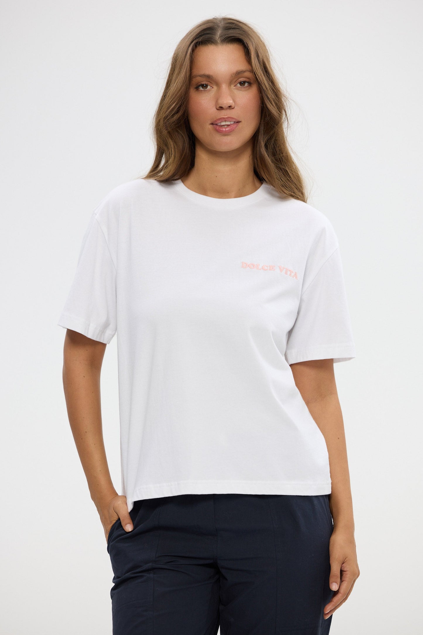 Woman wearing a white t-shirt with a small logo on a plain background
