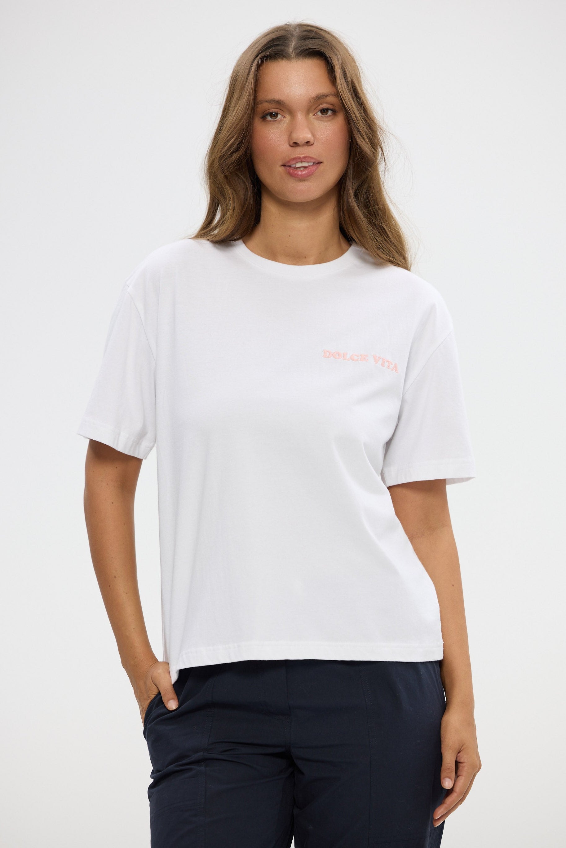 Woman wearing a white t-shirt with a small logo on a plain background