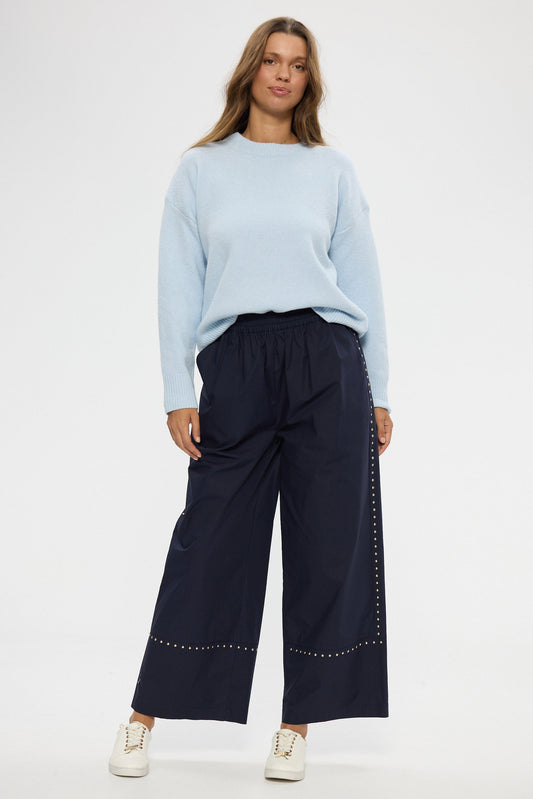 Woman wearing a light blue sweater and navy wide-leg pants with a white background