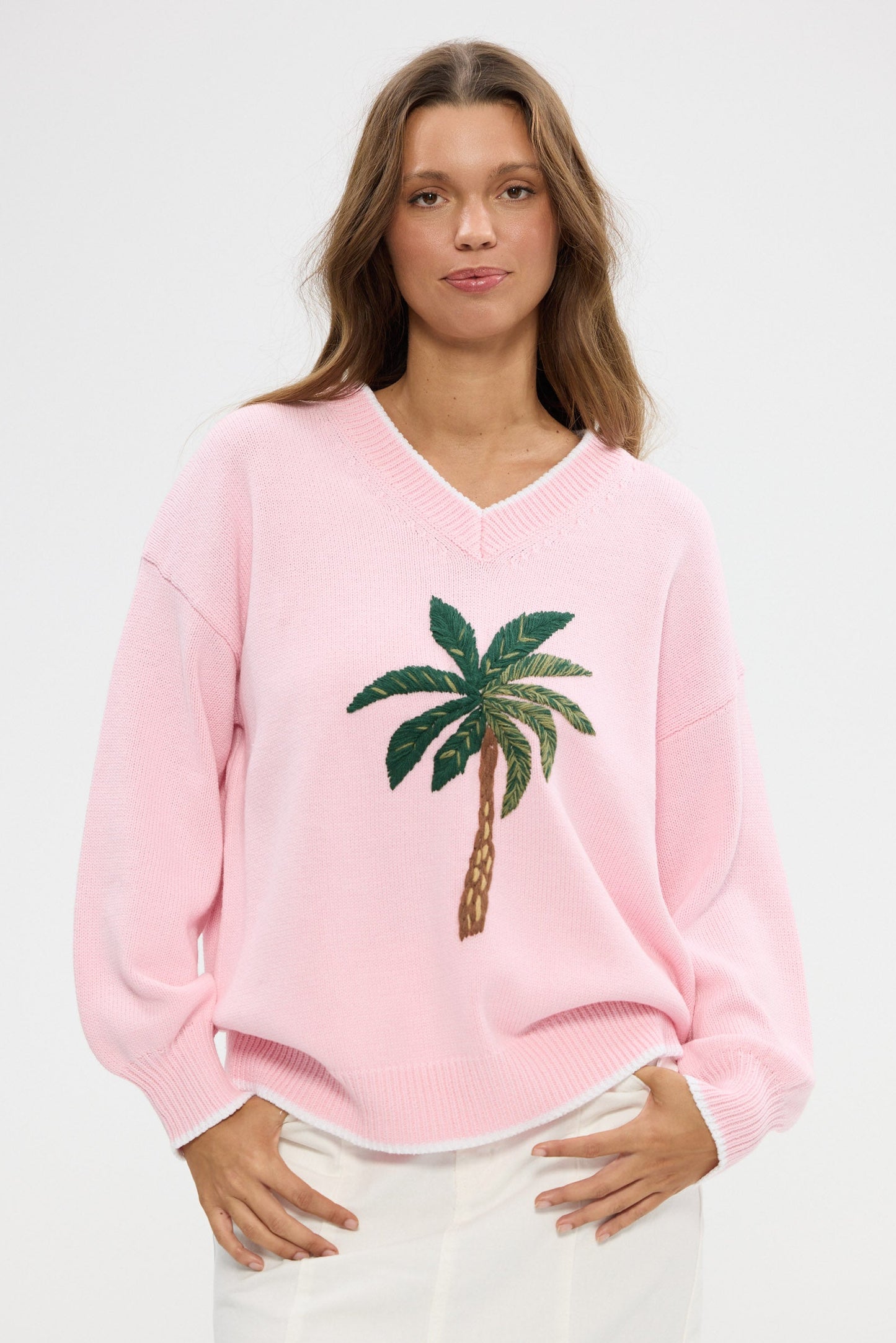 Woman wearing a pink sweater with a palm tree design on a white background
