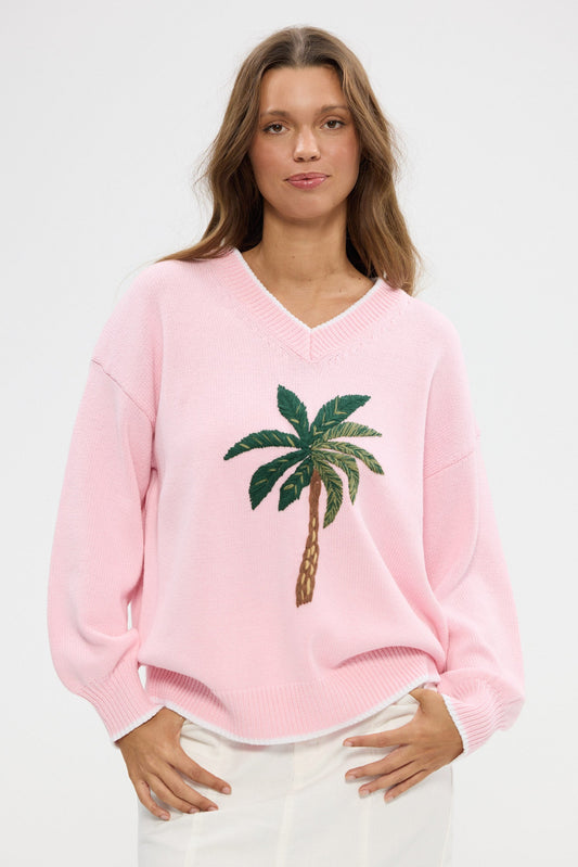 Woman wearing a pink sweater with a palm tree design on a white background
