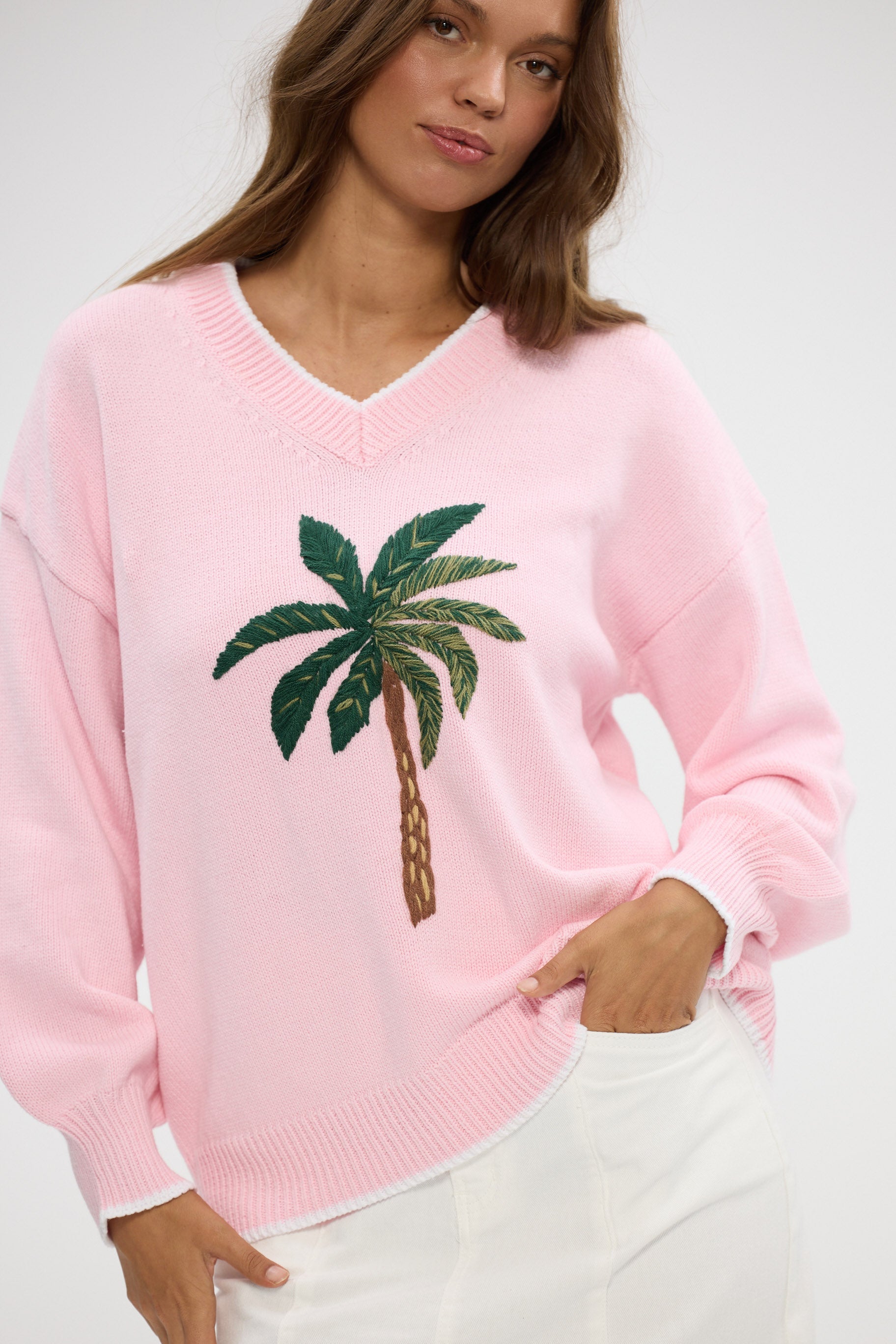 Woman wearing a pink sweater with a palm tree design on a white background
