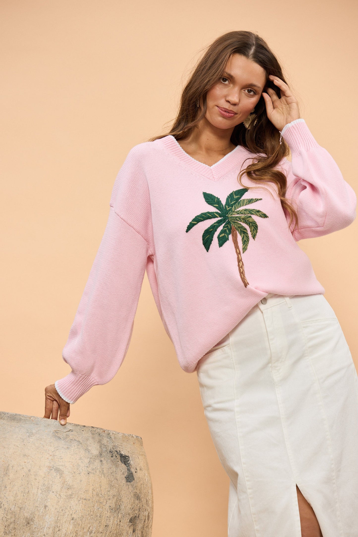 Woman wearing a pink sweater with a palm tree design against a beige background
