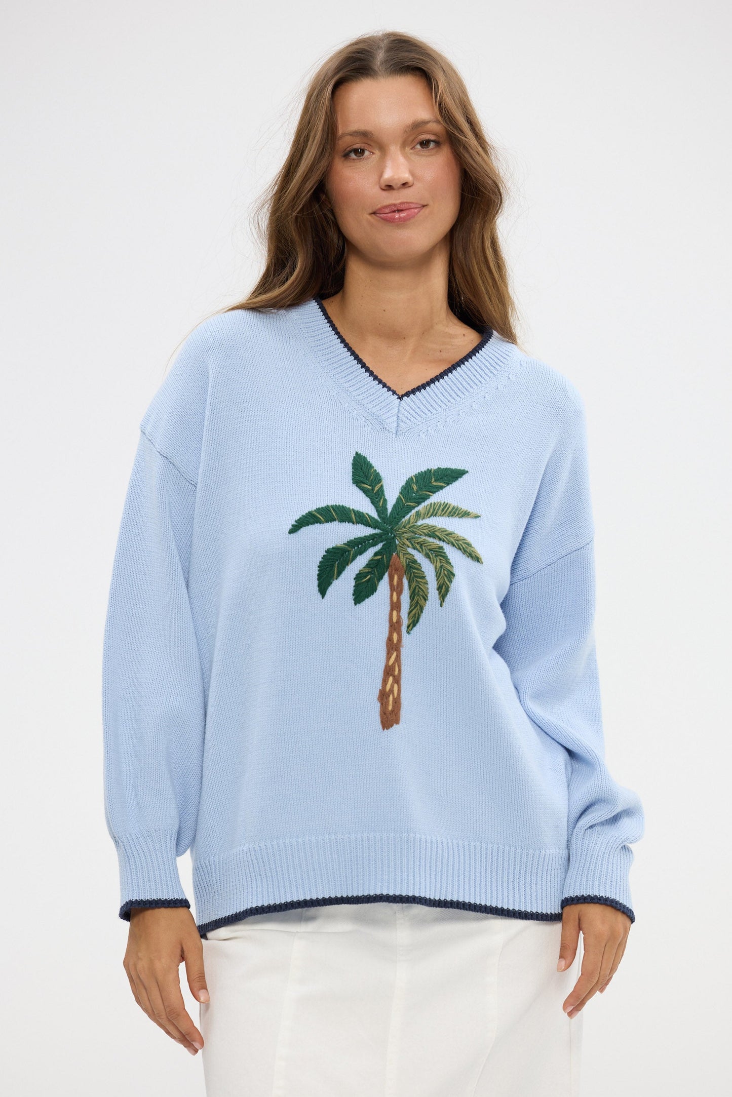 Woman wearing a light blue sweater with a palm tree design on a white background