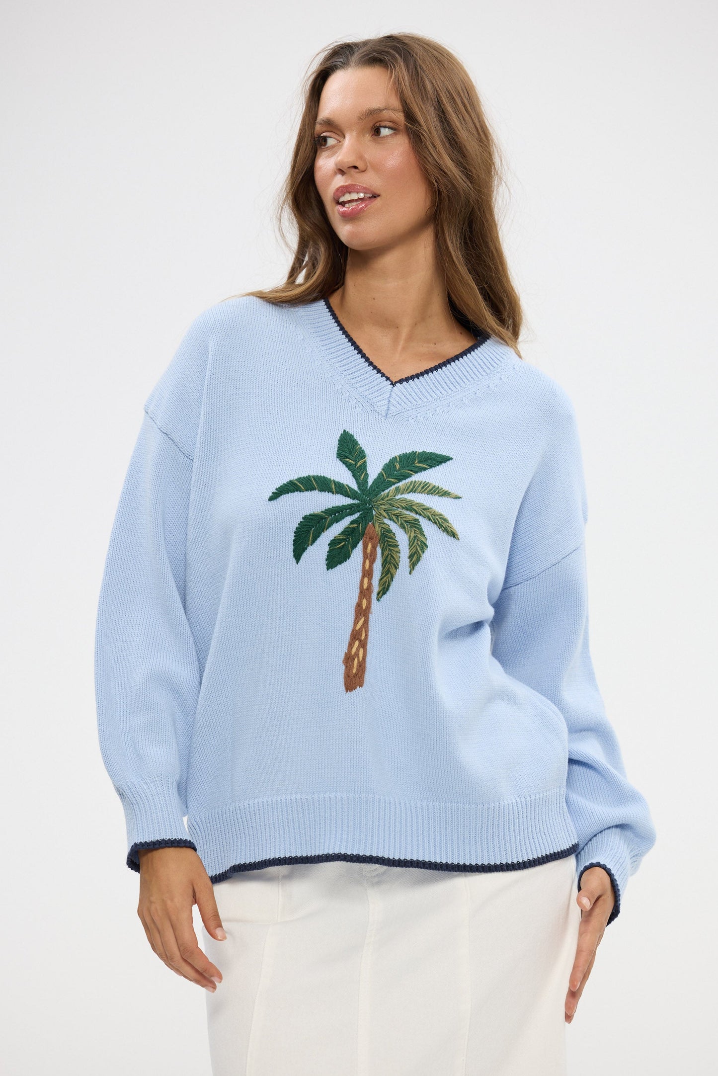 Woman wearing a light blue sweater with a palm tree design on a white background