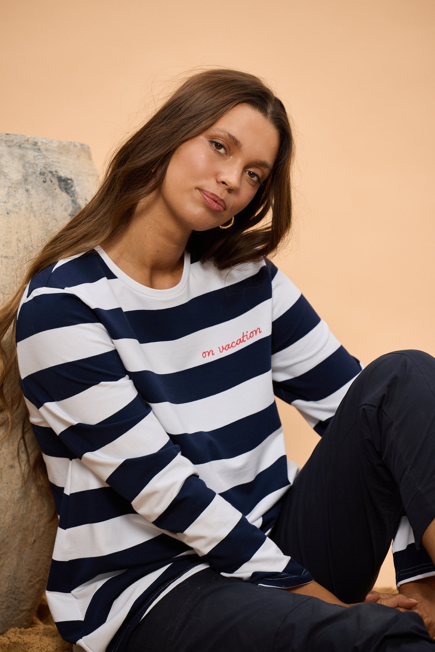 Woman wearing a navy and white striped sweater with text, sitting against a beige background