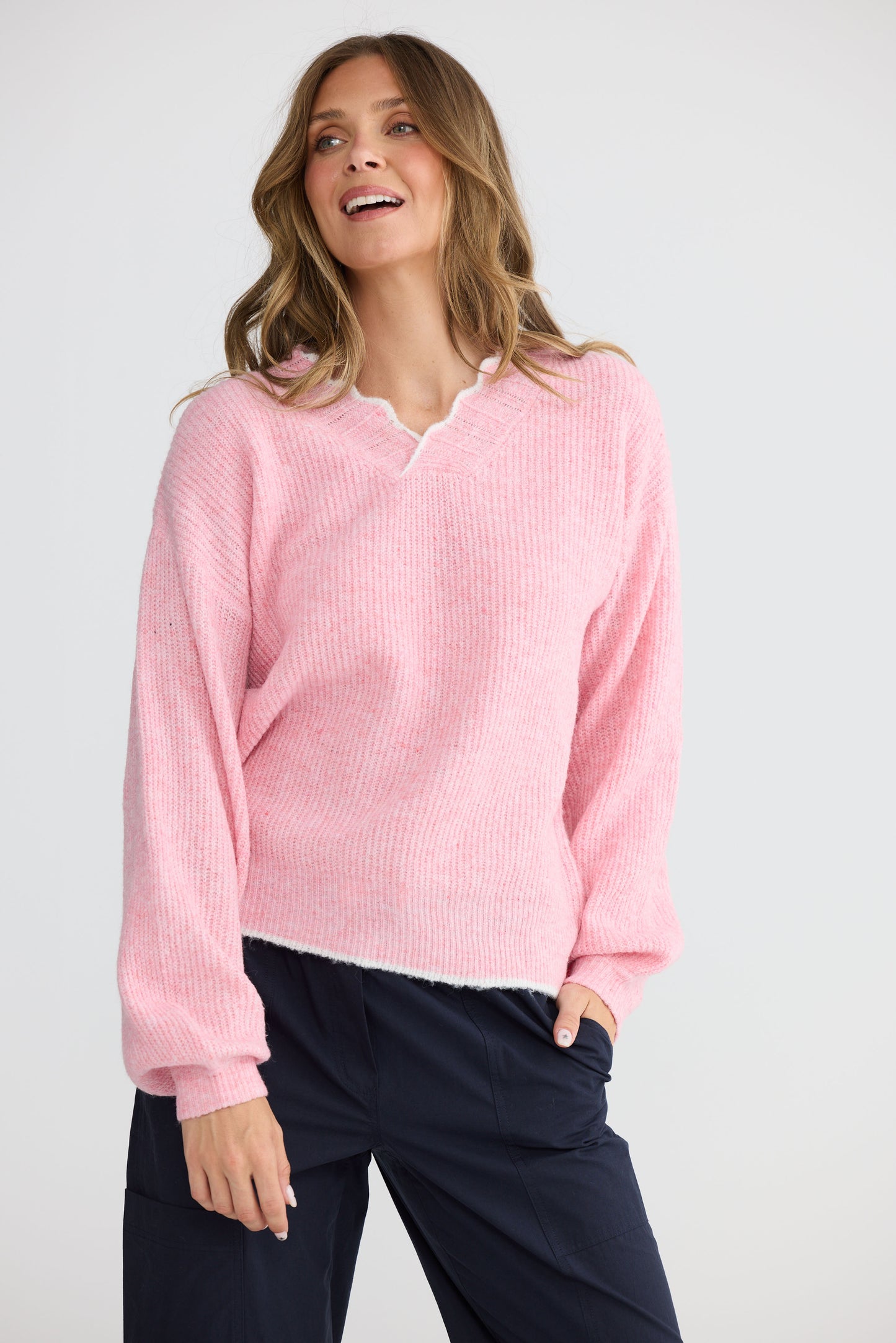 Model wearing Ocean Knit Pink with scalloped V-neckline, side view on white background