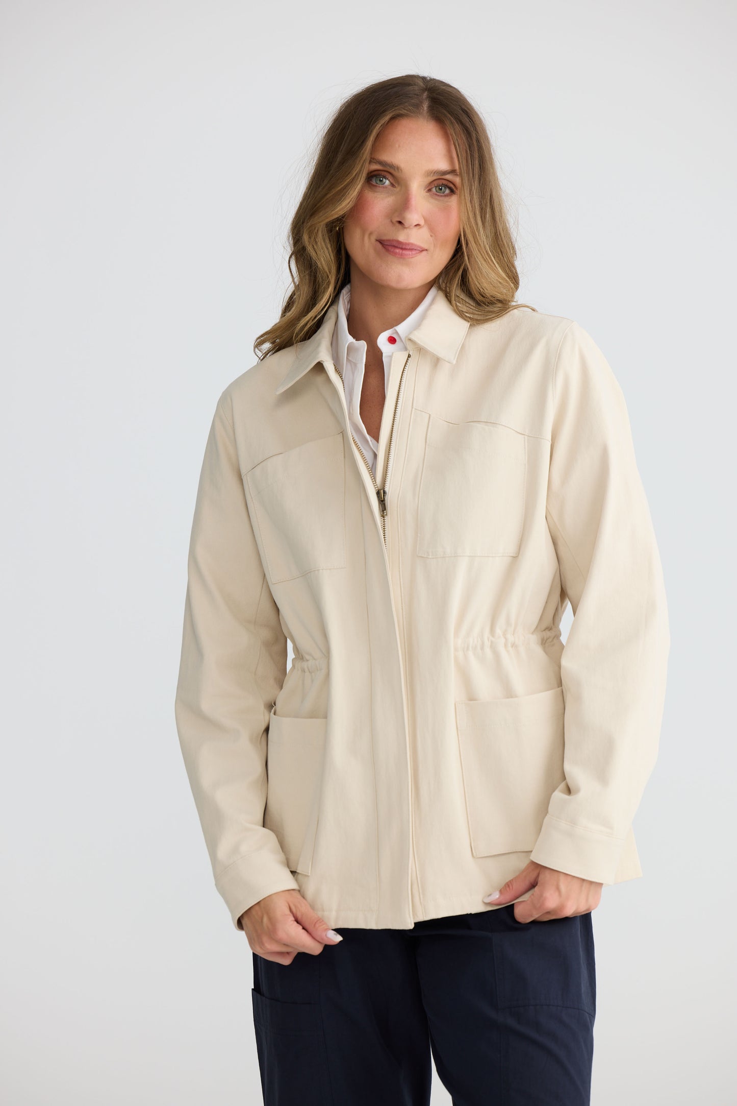 Model wearing Sabbia Jacket Cream with concealed zip and waist drawcord, full-length view on white background