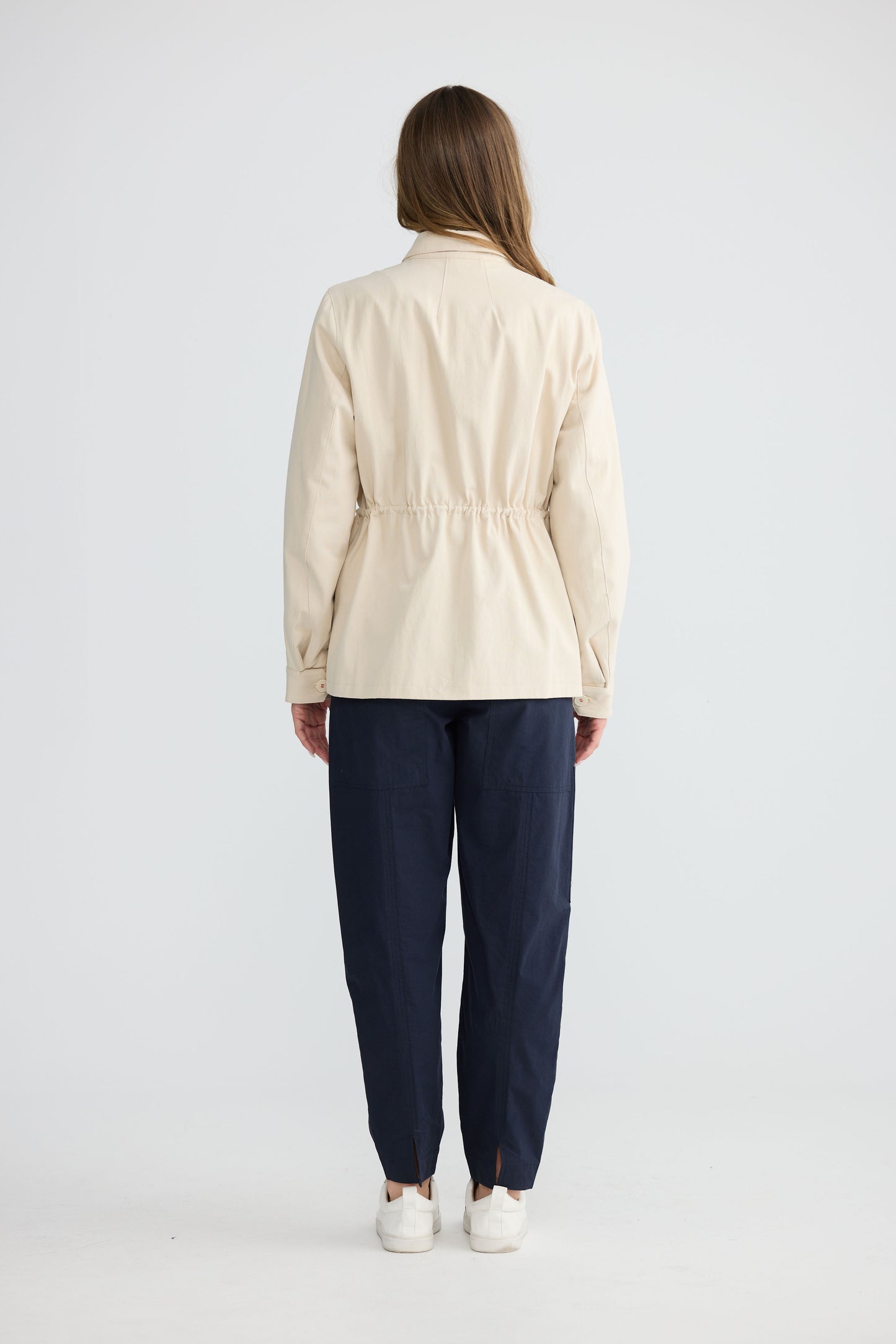 Model wearing Sabbia Jacket Cream with concealed zip and waist drawcord, detail view on white background