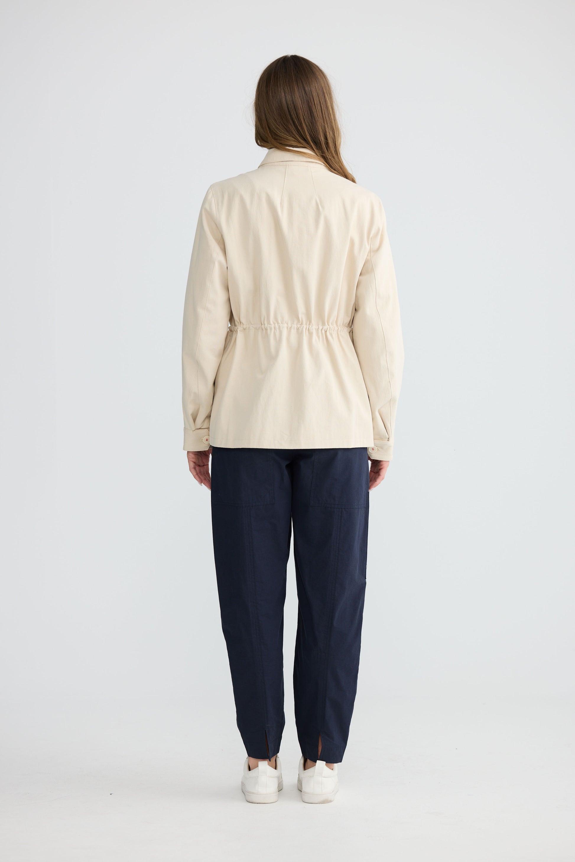 Model wearing Sabbia Jacket Cream with concealed zip and waist drawcord, detail view on white background