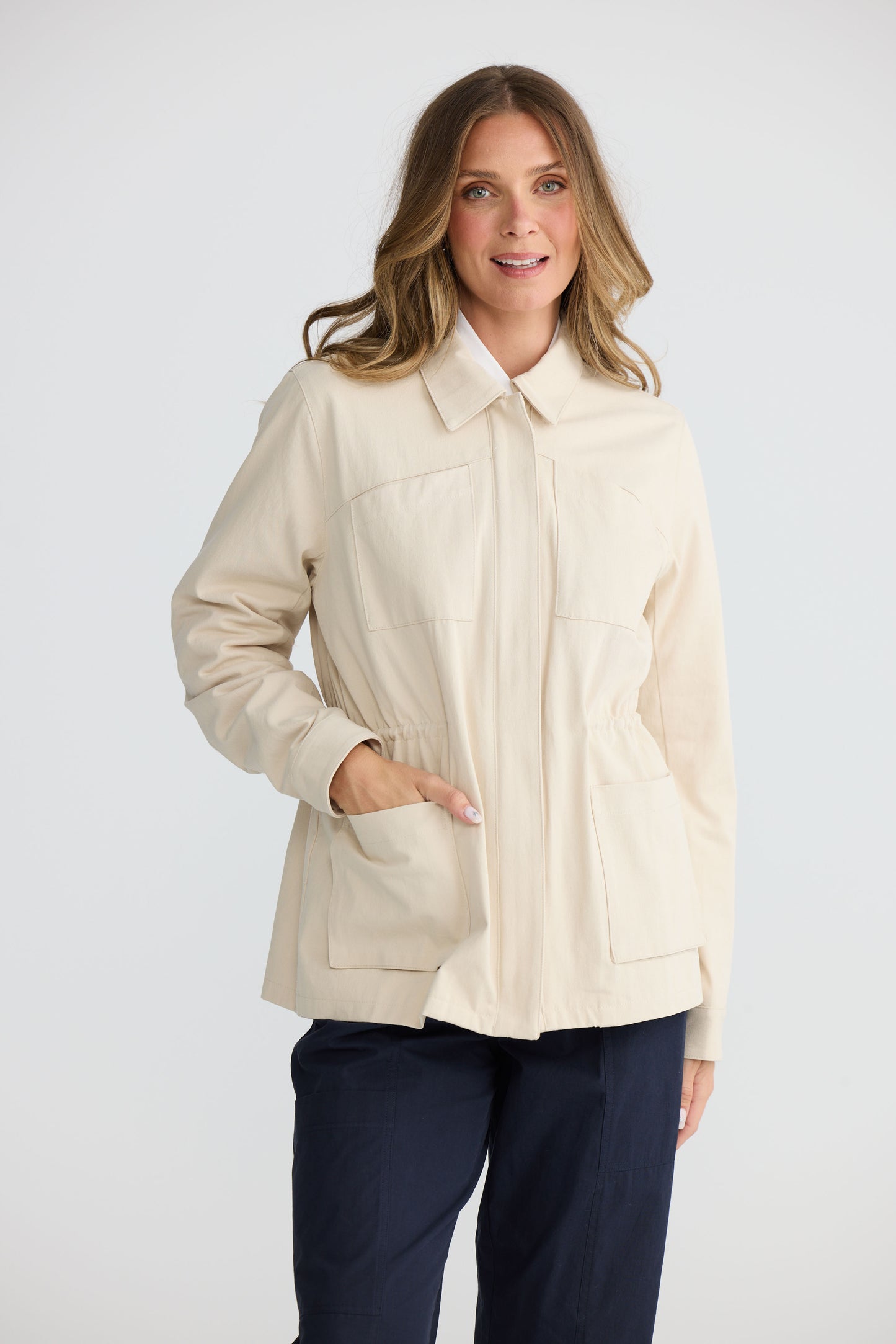 Model wearing Sabbia Jacket Cream with concealed zip and waist drawcord, front view on white background