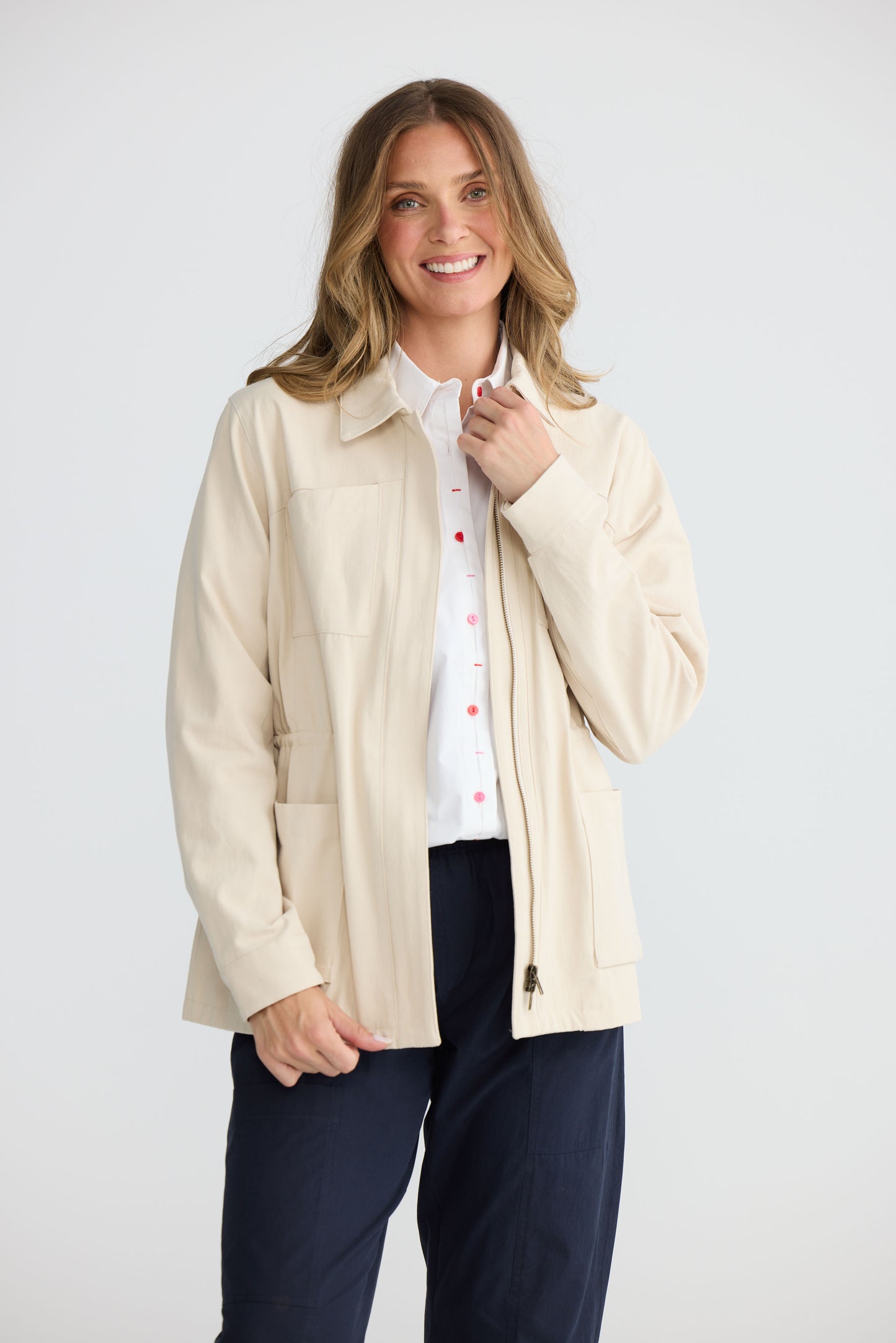 Model wearing Sabbia Jacket Cream with concealed zip and waist drawcord, back view on white background