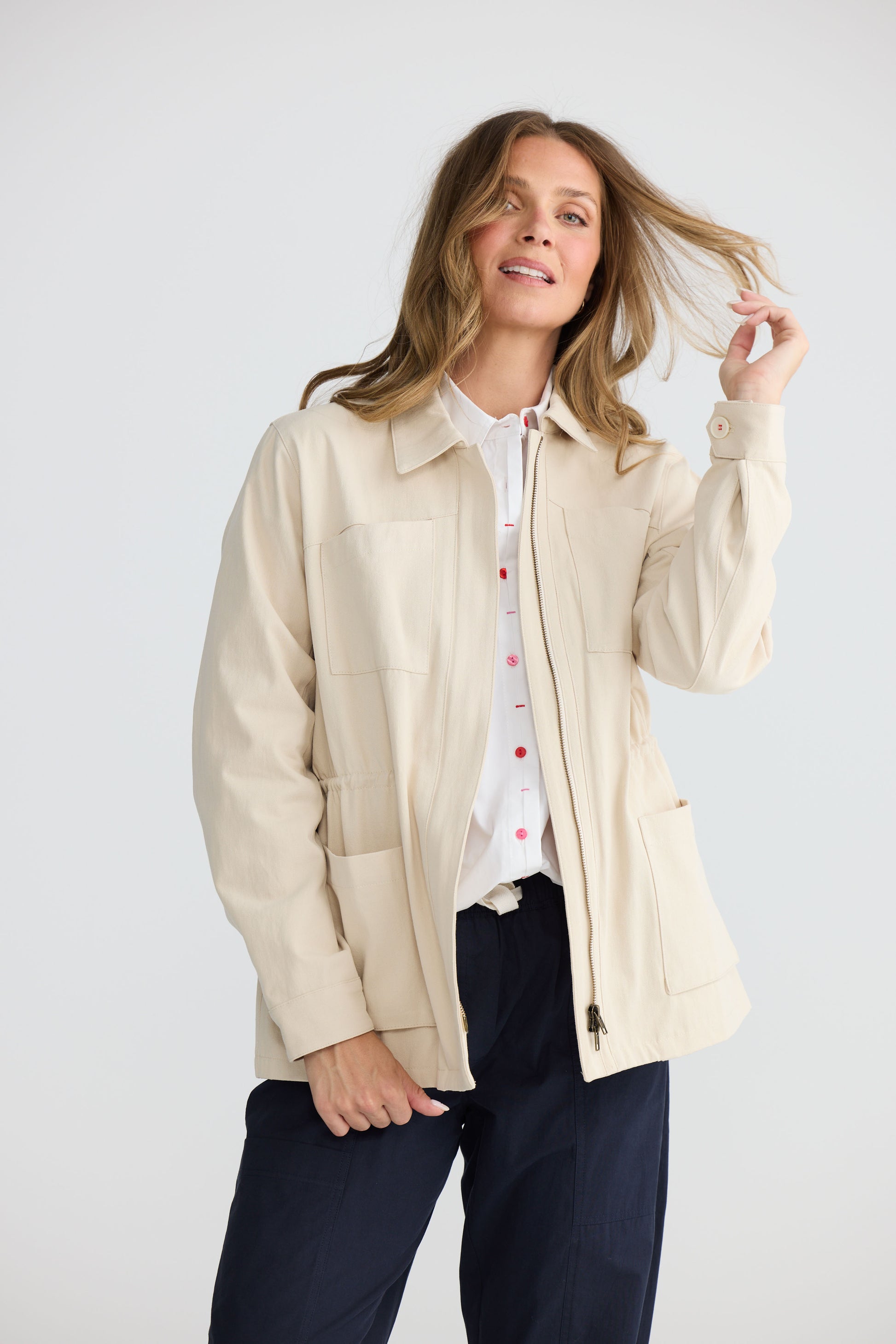 Model wearing Sabbia Jacket Cream with concealed zip and waist drawcord, side view on white background