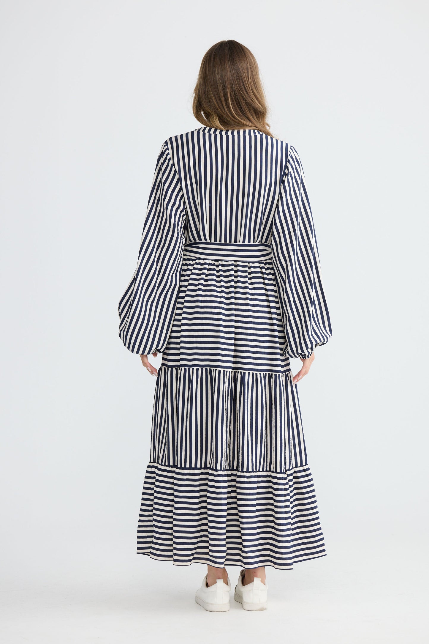 Model wearing Marla Dress Navy and White Stripe with balloon sleeves and waist tie, full-length view on white background
