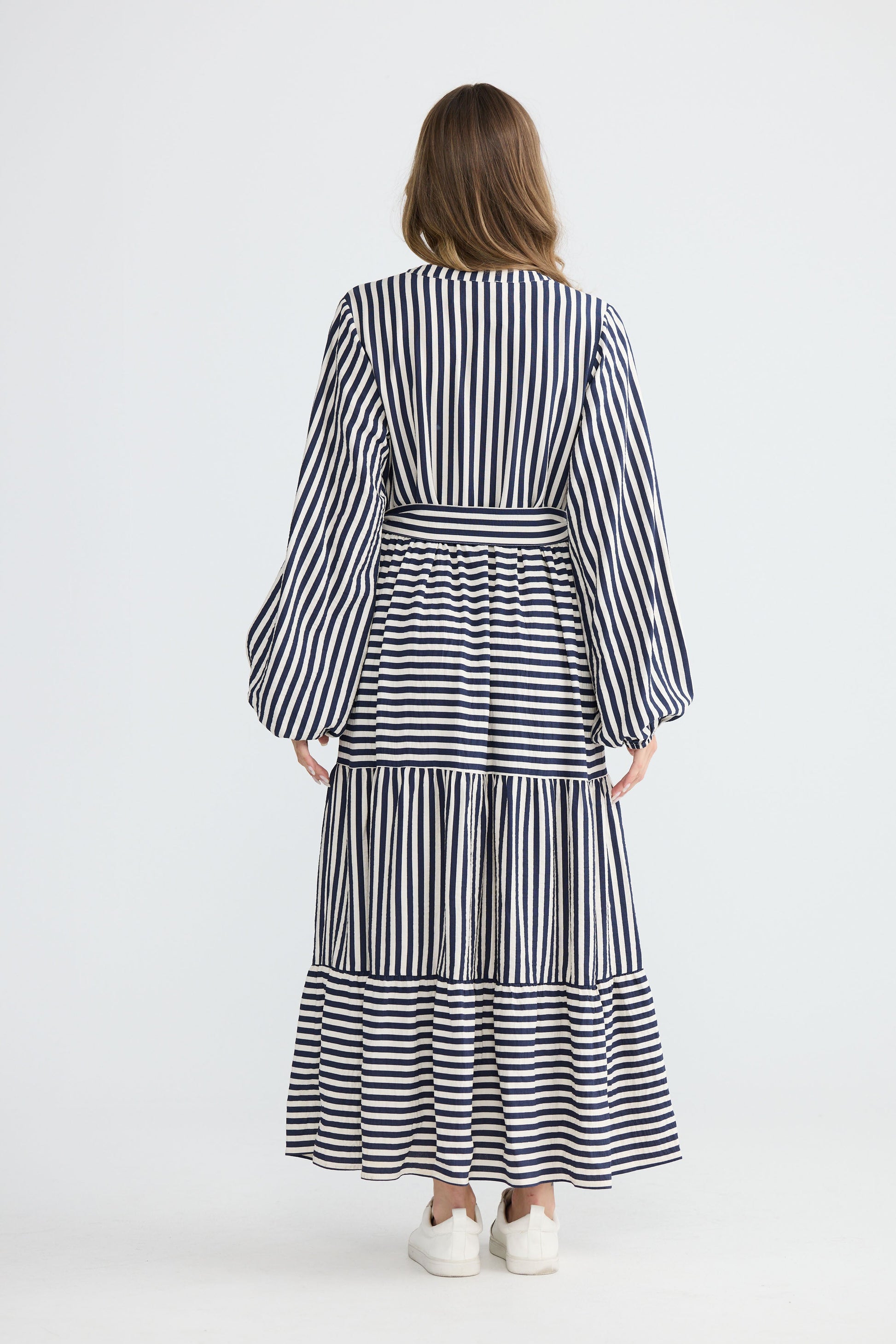 Model wearing Marla Dress Navy and White Stripe with balloon sleeves and waist tie, full-length view on white background