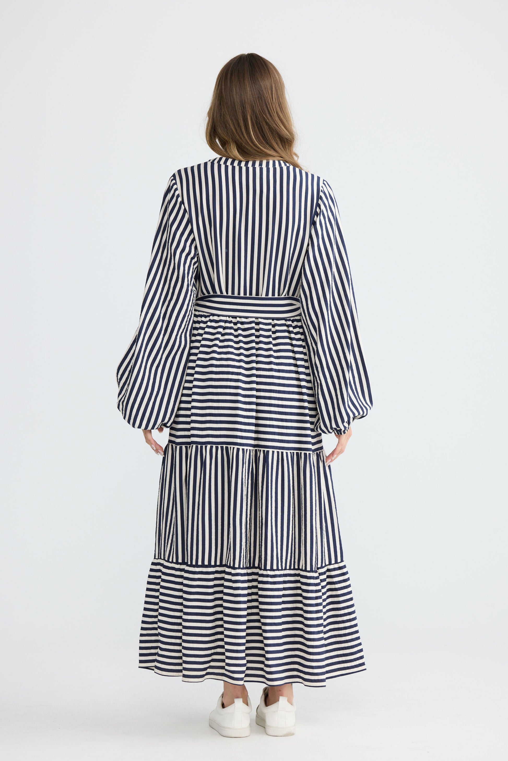 Model wearing Marla Dress Navy and White Stripe with balloon sleeves and waist tie, studio detail view on white background