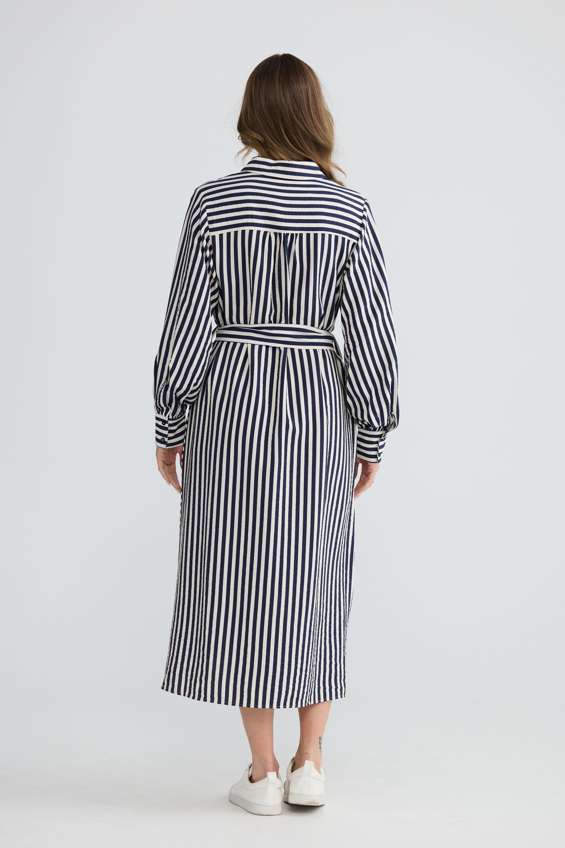 Model wearing Carnation Shirt Dress Navy and White Stripe with waist tie and in-seam pockets, side view on white background