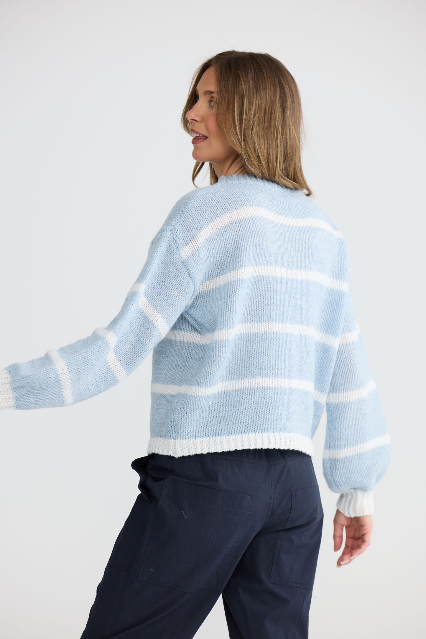 Model wearing Bay Knit Blue Stripe with ribbed trims and relaxed fit, side view on white background