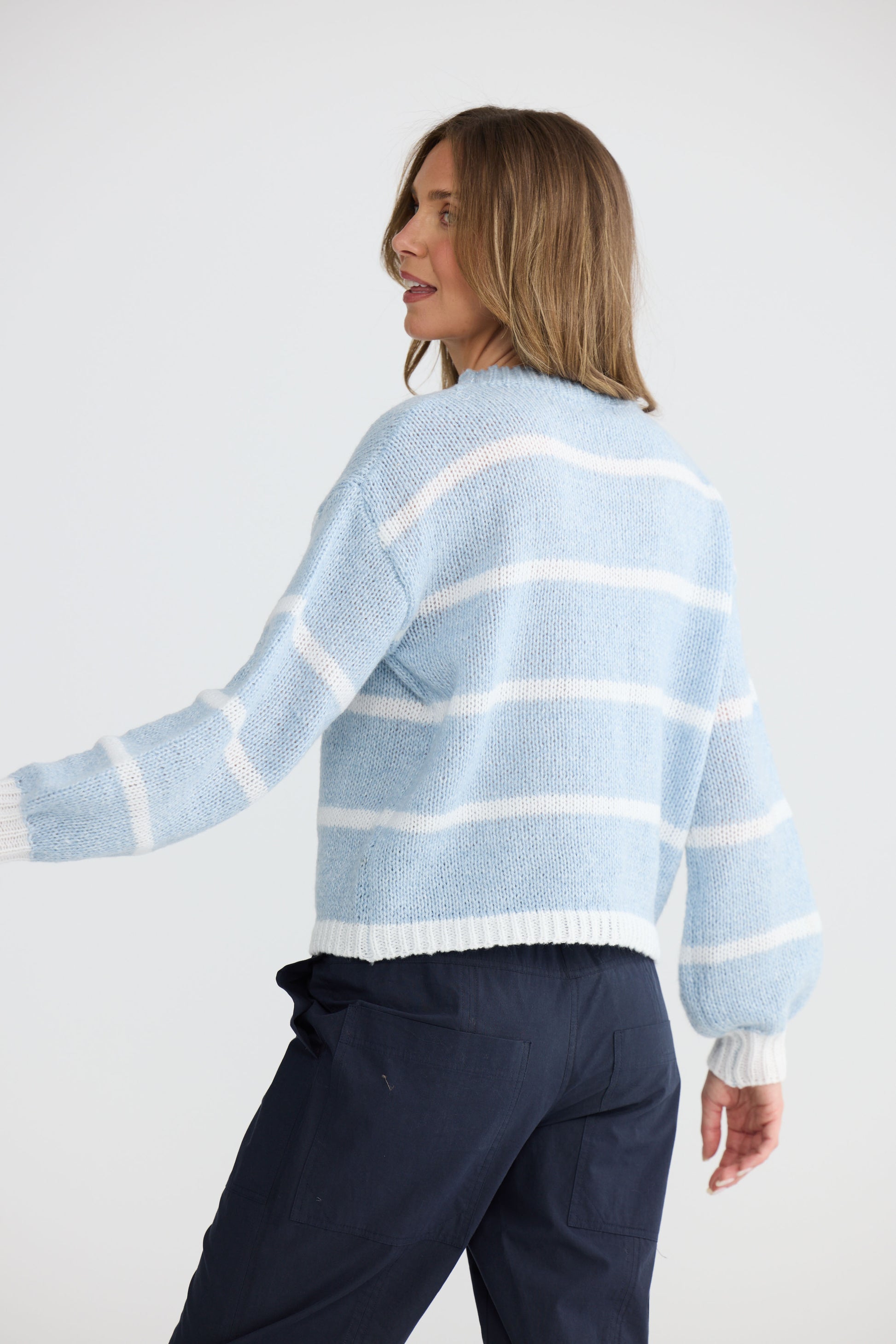 Model wearing Bay Knit Blue Stripe with ribbed trims and relaxed fit, side view on white background