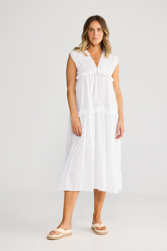 Model wearing Behati Dress in white, front view. Gathered shoulders, V-neckline, tiered midi with frill seams.