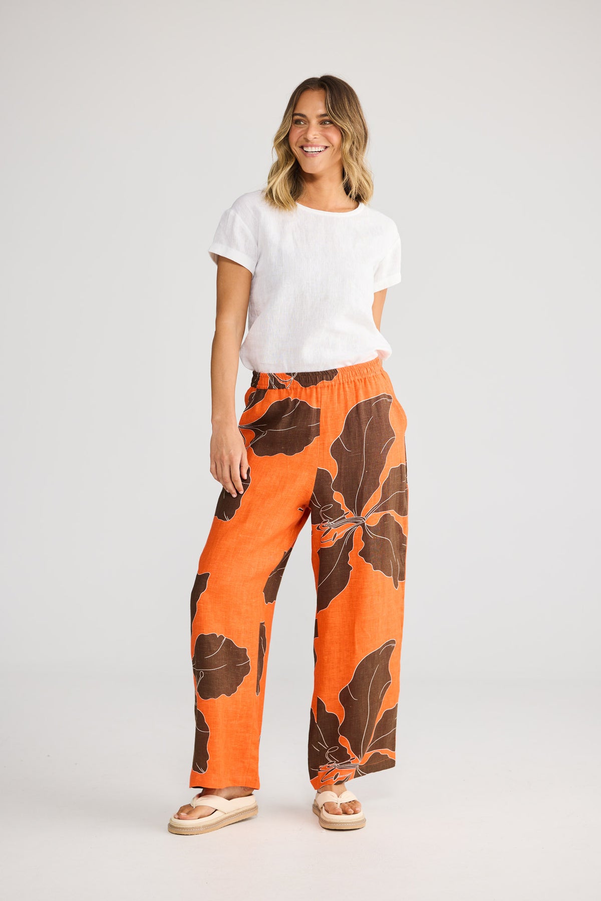 Model wearing Playa Pant in hibiscus breeze, front view. Relaxed wide leg, elasticated waist, orange-and-brown leaf print.