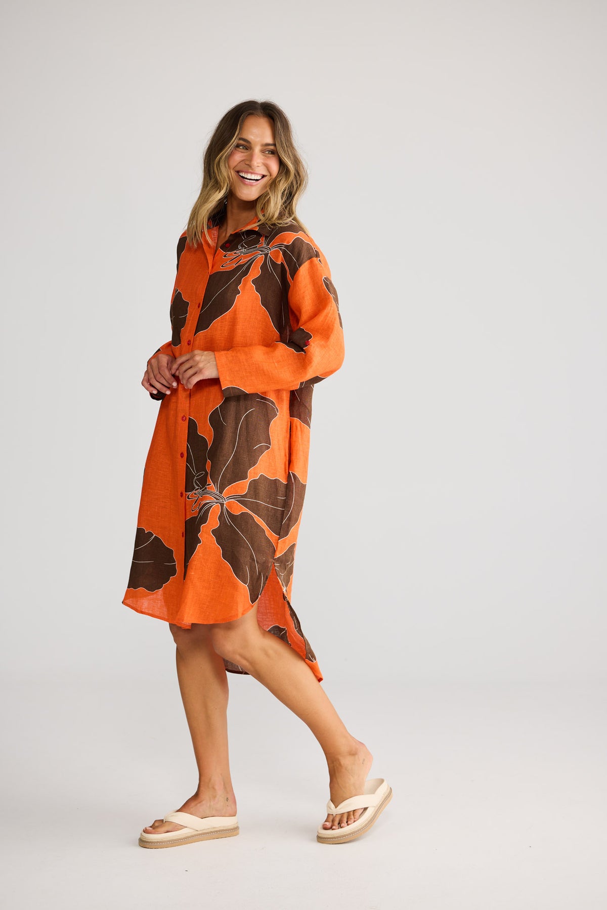 Model wearing Sunny Overshirt in hibiscus breeze, front view. Relaxed shirt dress, button front, orange-and-brown leaf print.