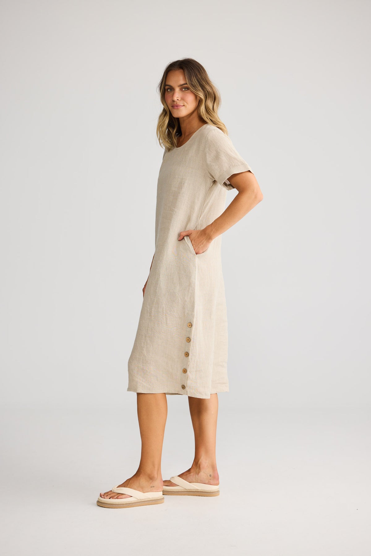 Model wearing Foreshore Dress in natural linen, front view. Round neckline, rolled cuff sleeve, straight silhouette.