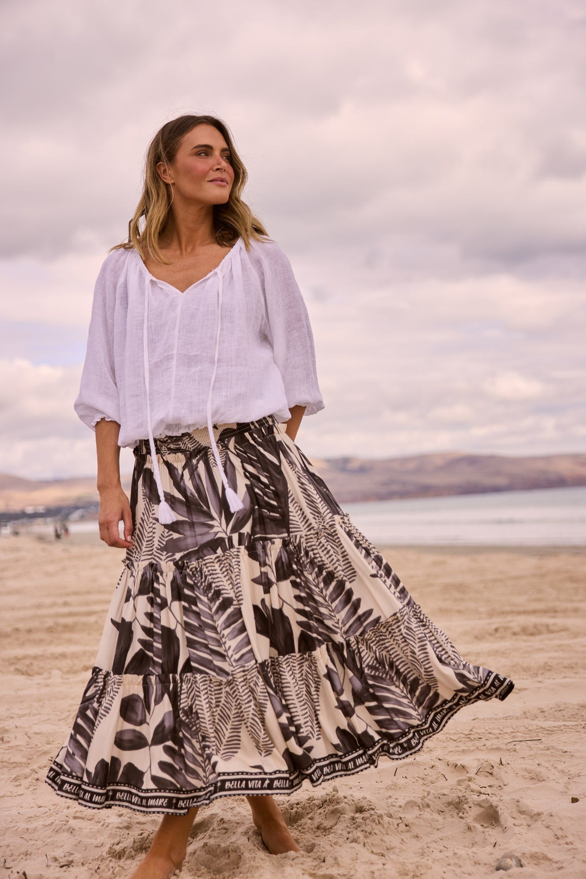Model wearing Seaside Top in white, front view. Tasselled neck tie, raglan sleeve, shirred cuff and waistband.