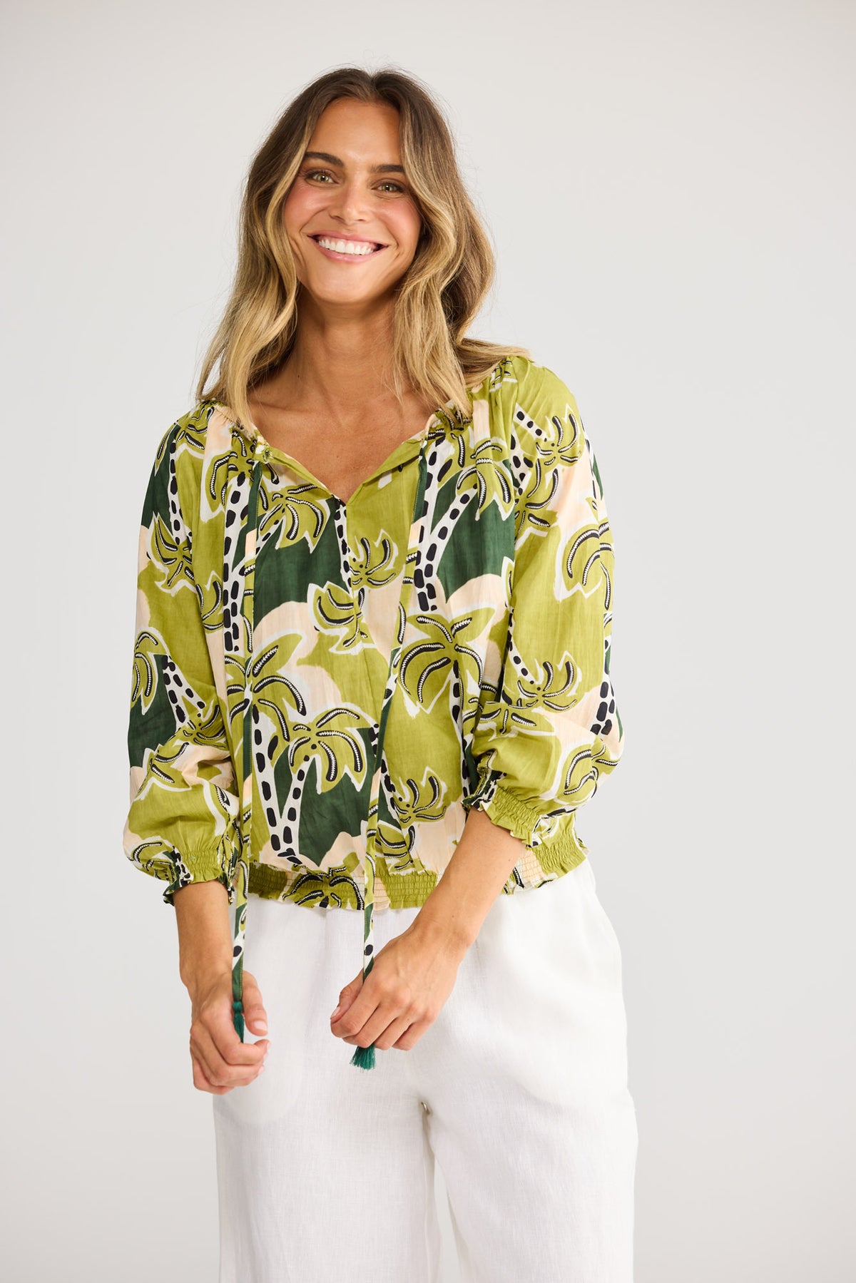 Model wearing Seaside Top in tropical deco, front view. Tasselled neck tie, raglan sleeve, green palm-tree print on cream.