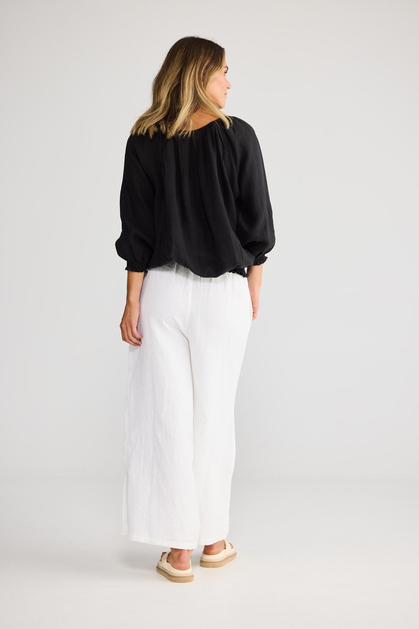Model wearing Seaside Top in black, front view. Tasselled neck tie, raglan sleeve, shirred cuff and waistband.