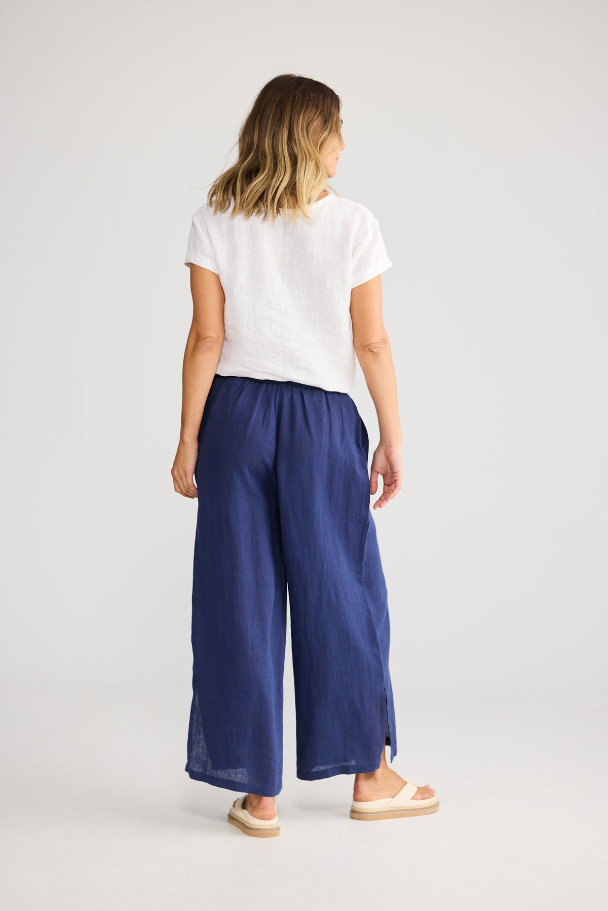 Model wearing Fly Away Pant in navy, front view. Relaxed wide leg, elasticated waistband, side split visible at hem.