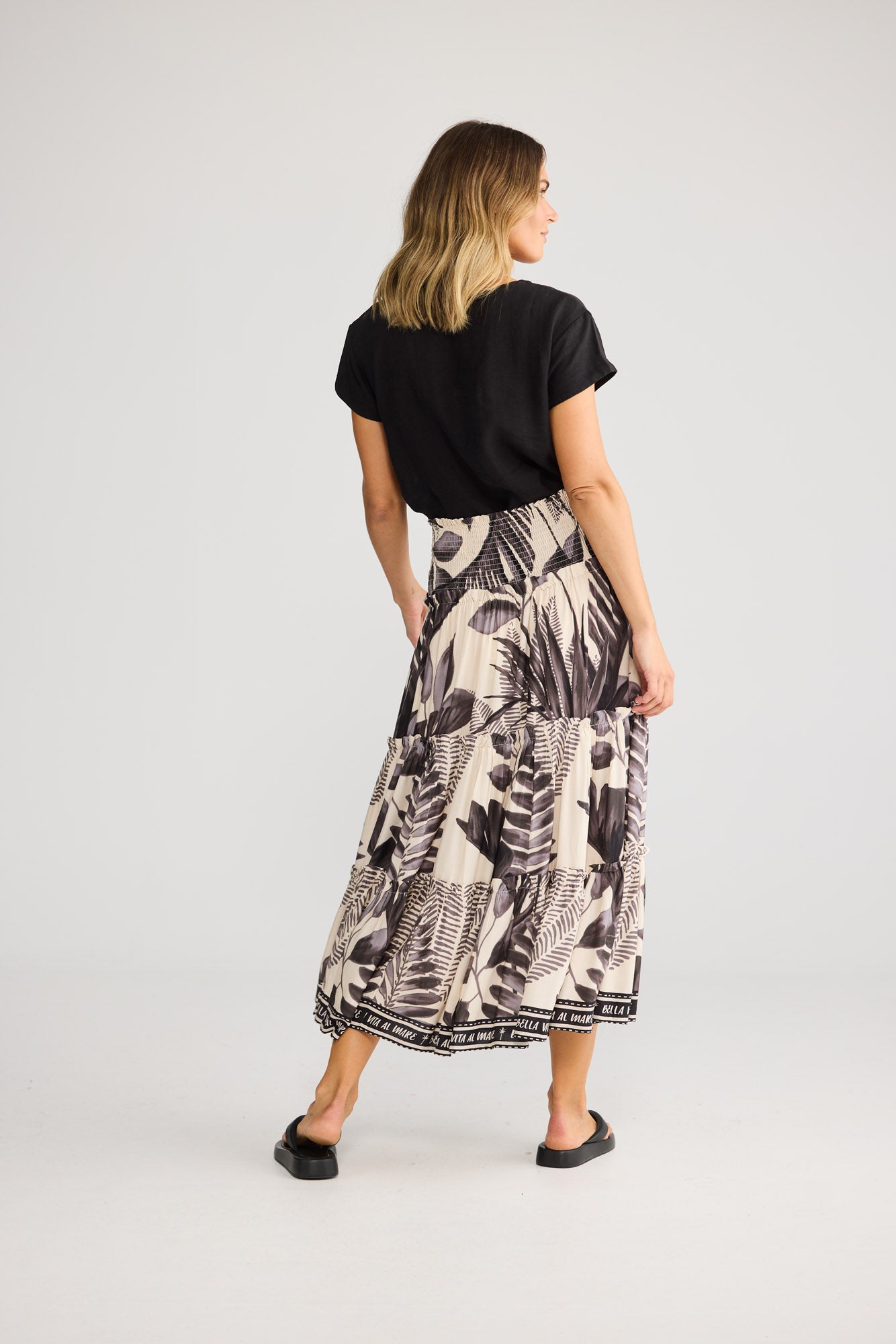 Model wearing Pier Skirt in sunset palm, front view. Shirred waist panel, tiered maxi with black-and-cream palm-leaf print.