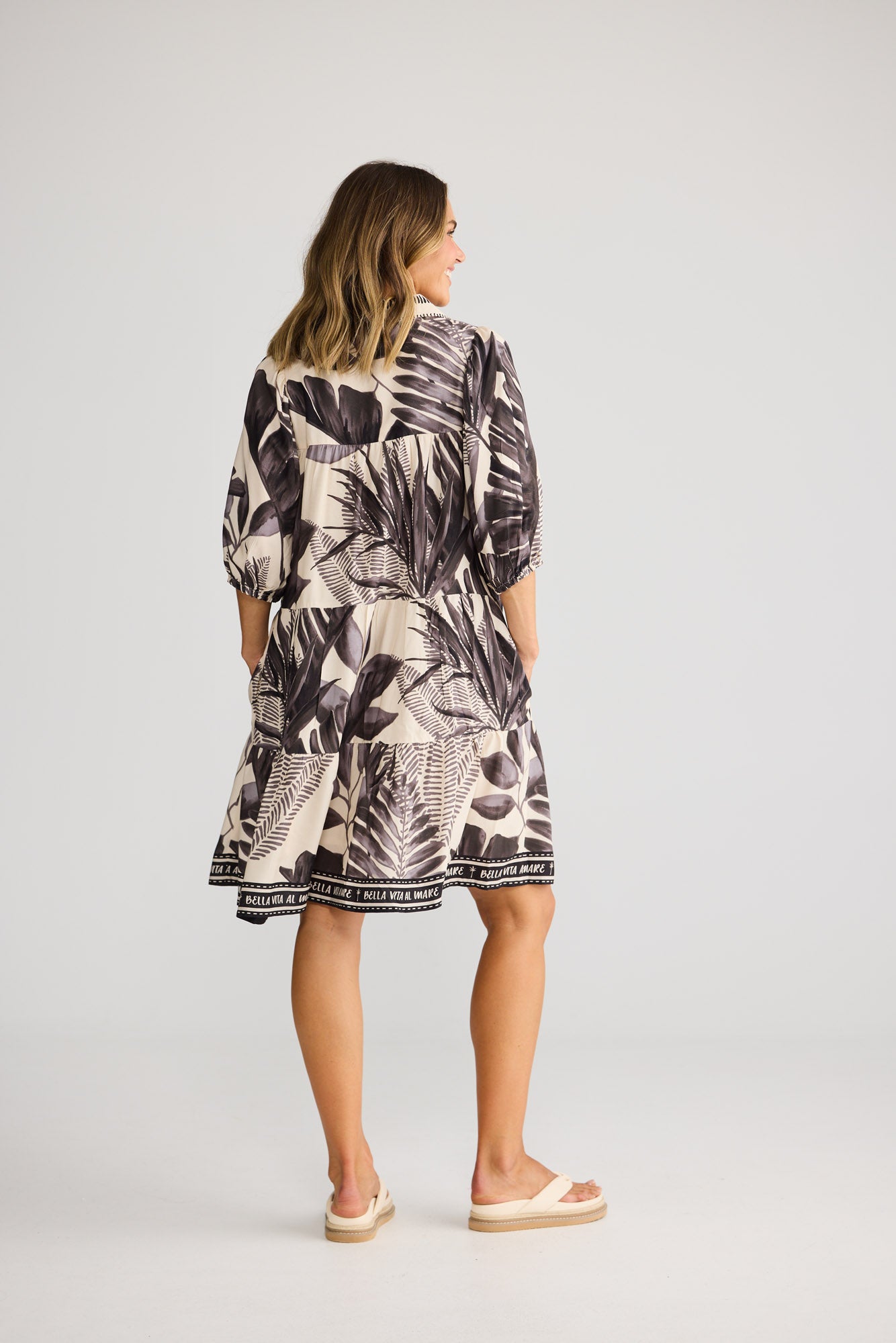 Model wearing Fiji Dress in sunset palm, front view. Collared, button front, elasticated sleeve, tiered border-print skirt.