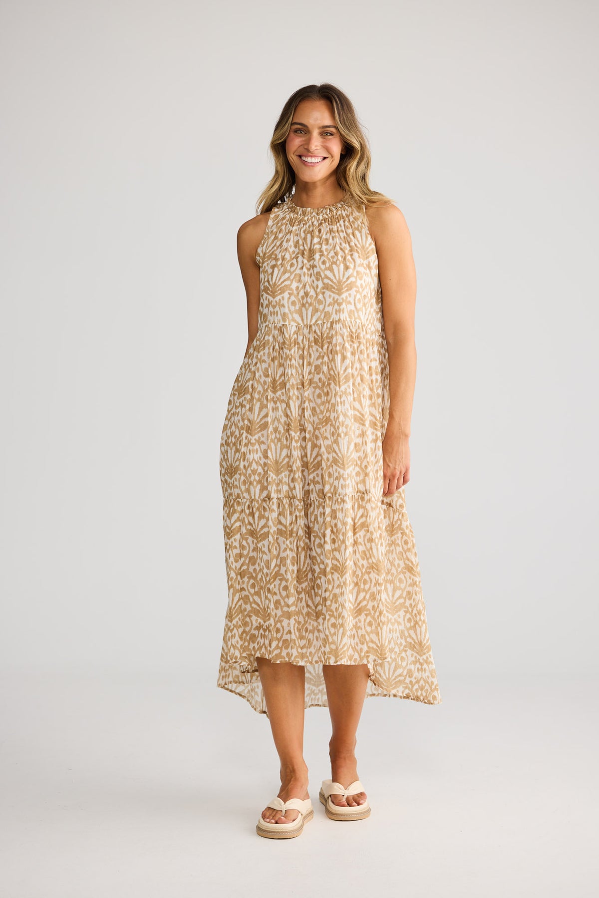 Model wearing Margot Dress in taupe spring fan, front view. Gathered halter, tiered hi-lo skirt, tan ikat fan print.