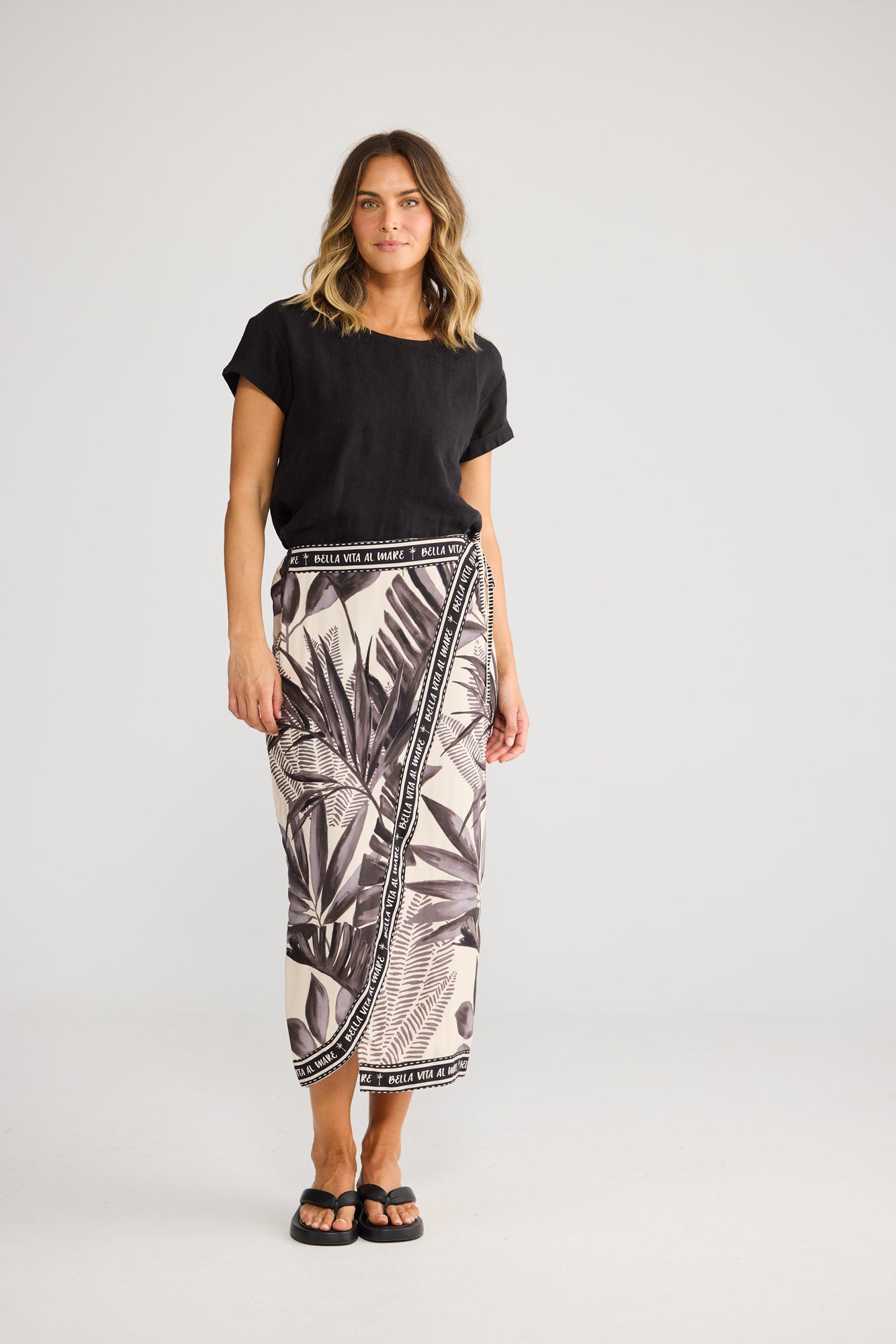 Model wearing Ocean Sarong Skirt in sunset palm, front view. Faux wrap style, side tie, black-and-cream palm-leaf print.