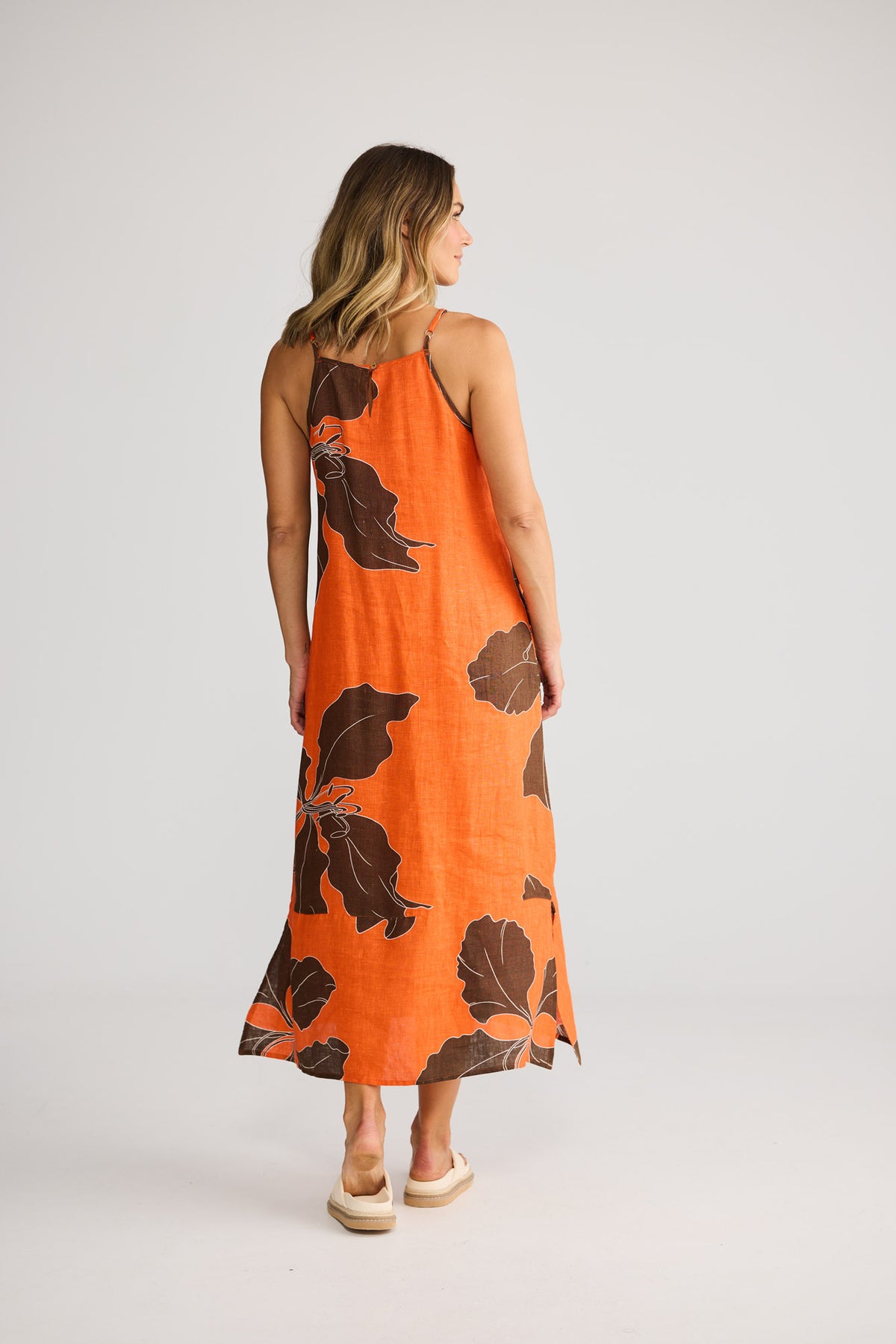 Model wearing Cliffside Maxi Dress in hibiscus breeze, front view. Spaghetti straps, side-seam buttons, large leaf print.