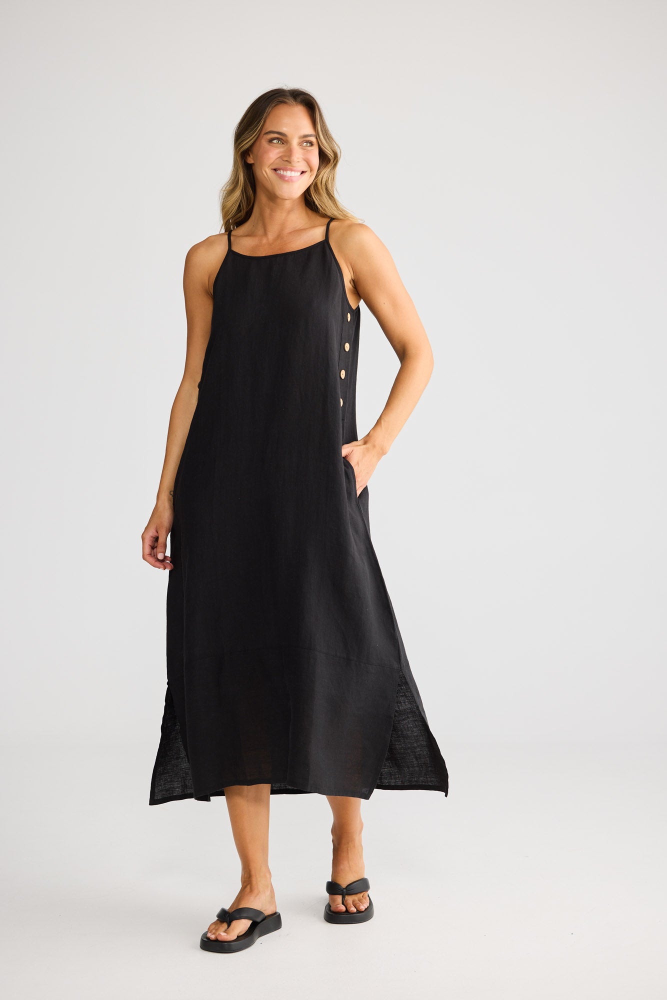 Model wearing Cliffside Maxi Dress in black, front view. Spaghetti straps, button detail down one side seam.