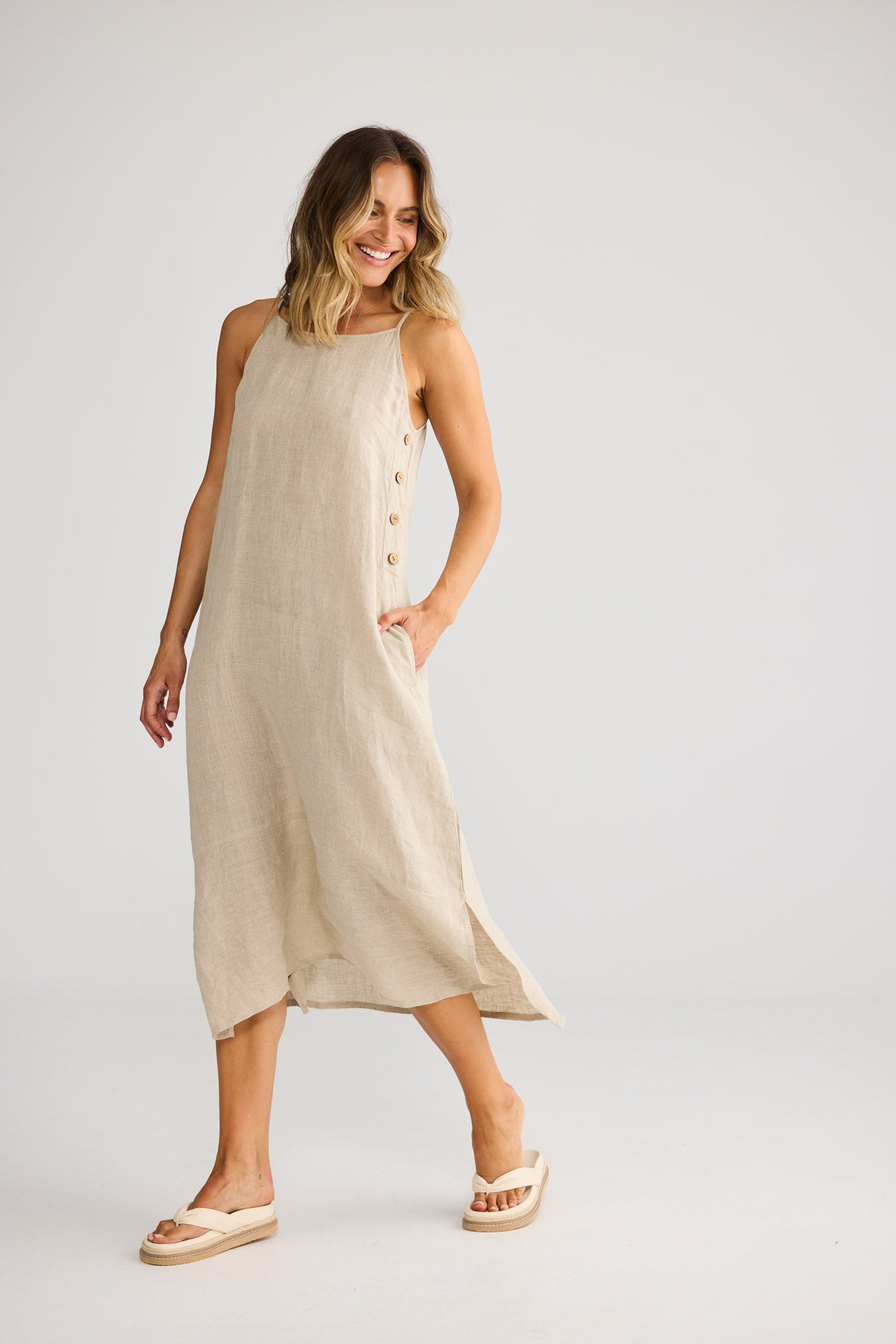 Model wearing Cliffside Maxi Dress in natural linen, front view. Spaghetti straps, button detail down one side seam.