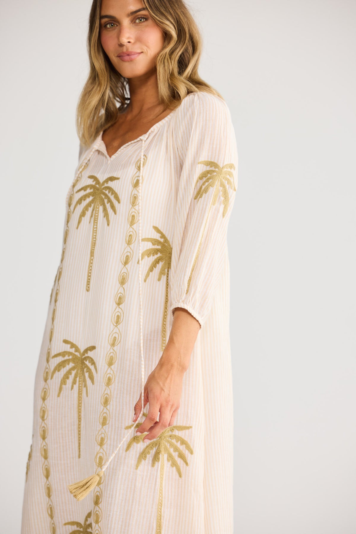 Model wearing Ohana Dress in natural stripe, front view. Neck ties, elasticated cuff sleeve, gold palm embroidery.