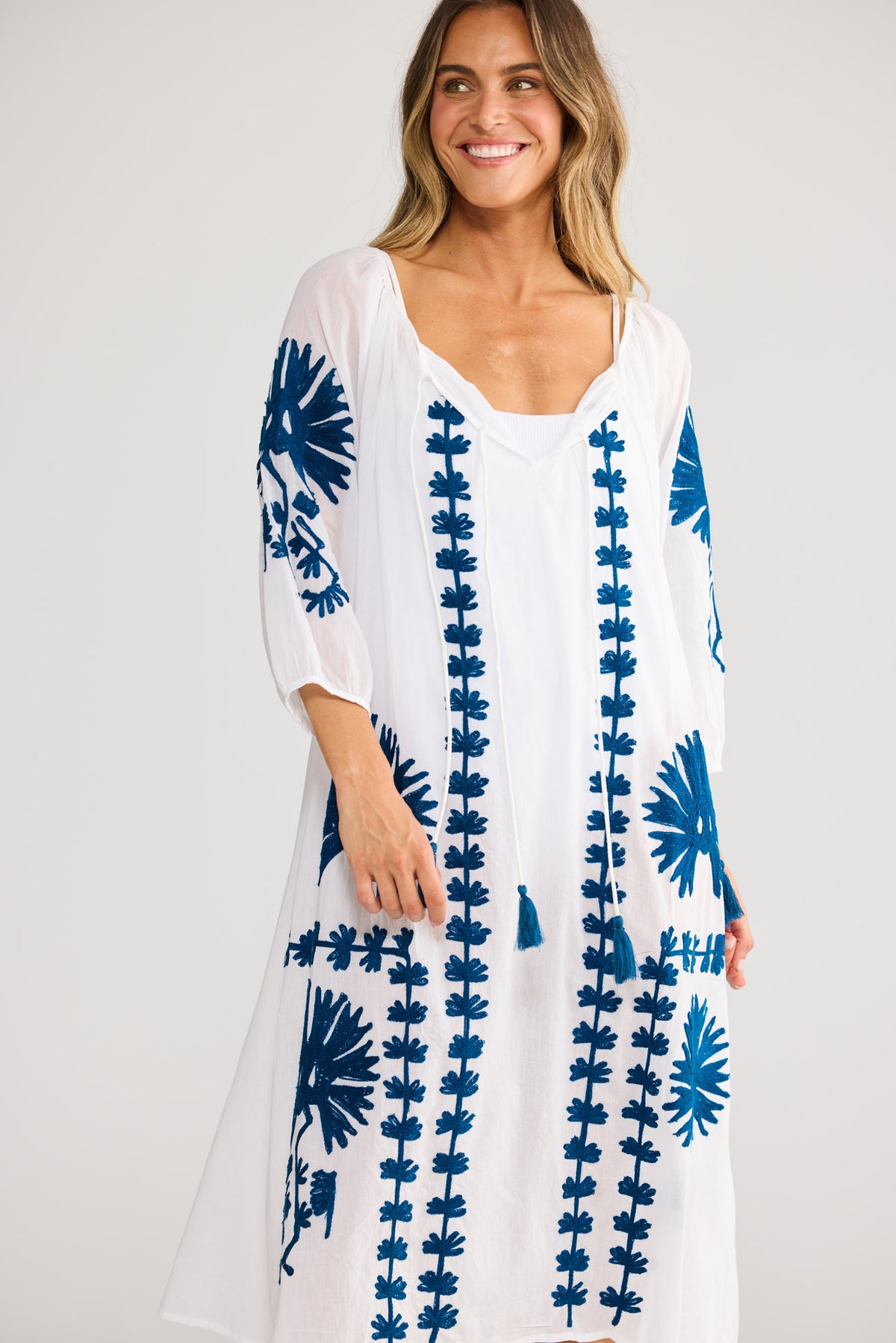 Model wearing Aloha Dress in white, front view. Sleeveless with gathered V-neckline and ruffle trim, tiered skirt.
