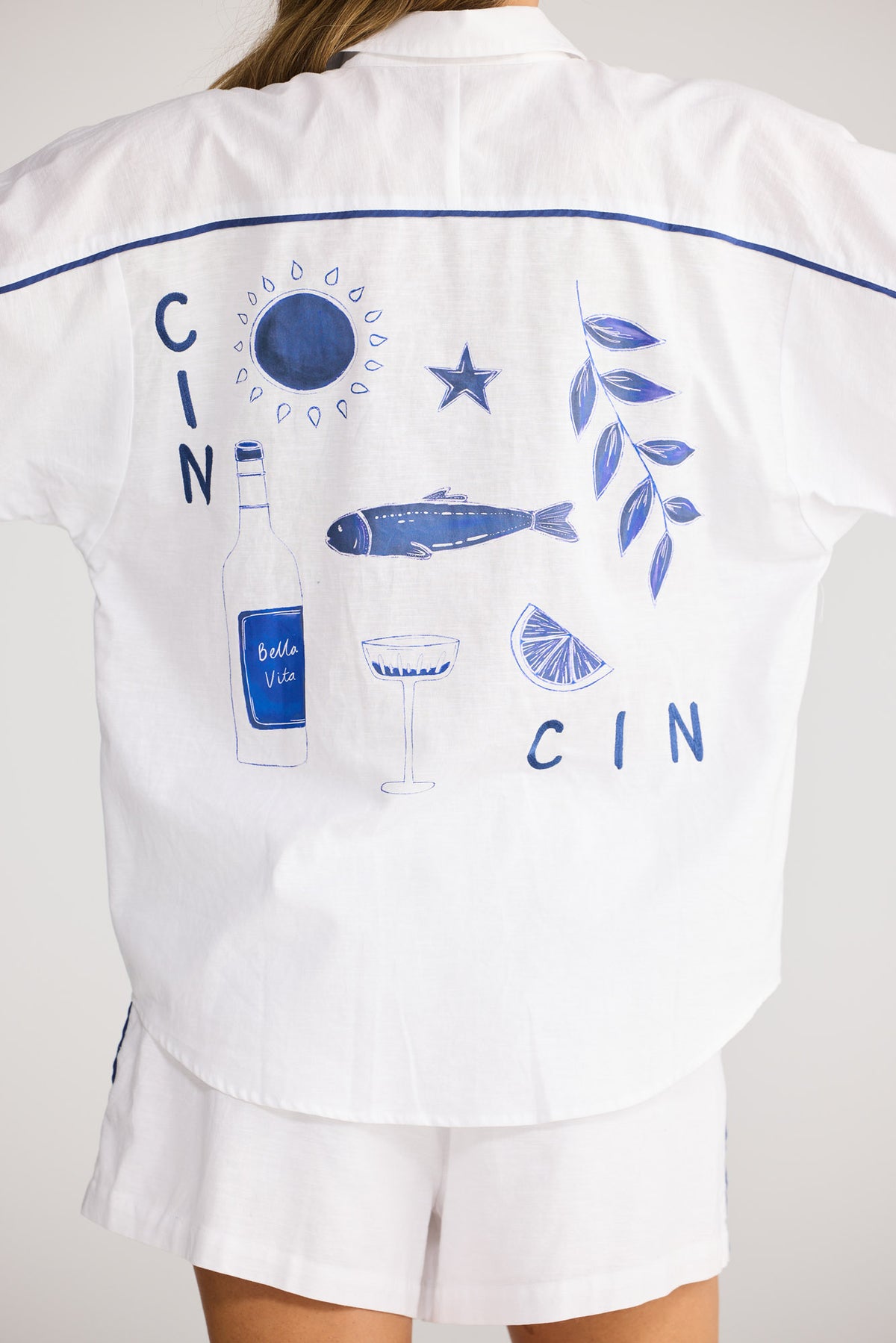 Model wearing Vacation Shirt in white, front view. Oversized collared shirt, navy piping, embroidered cocktail motif pocket.