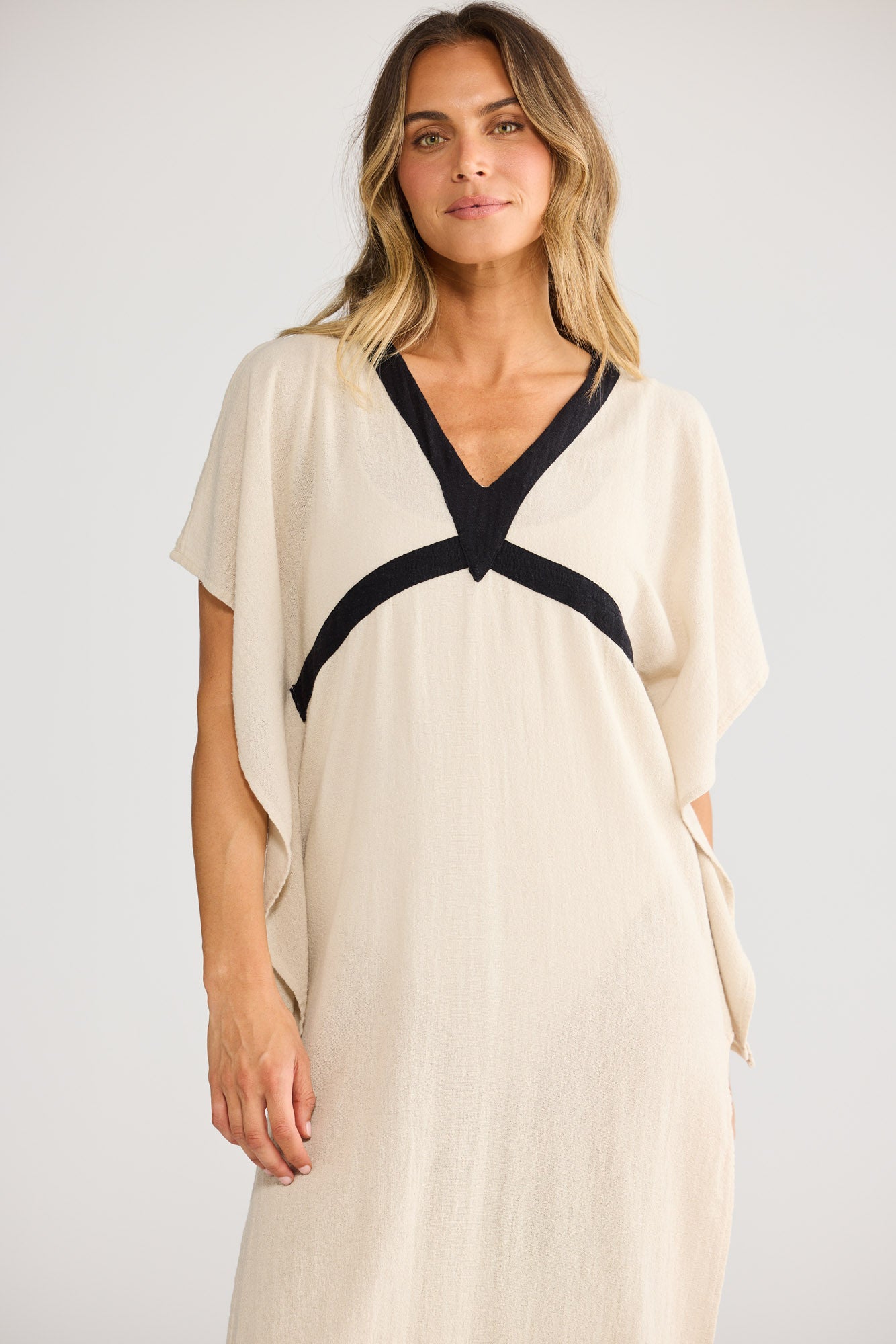 Model wearing Luma Kaftan in natural with black, front view. Dolman sleeve, V-neck with black trim, side split.