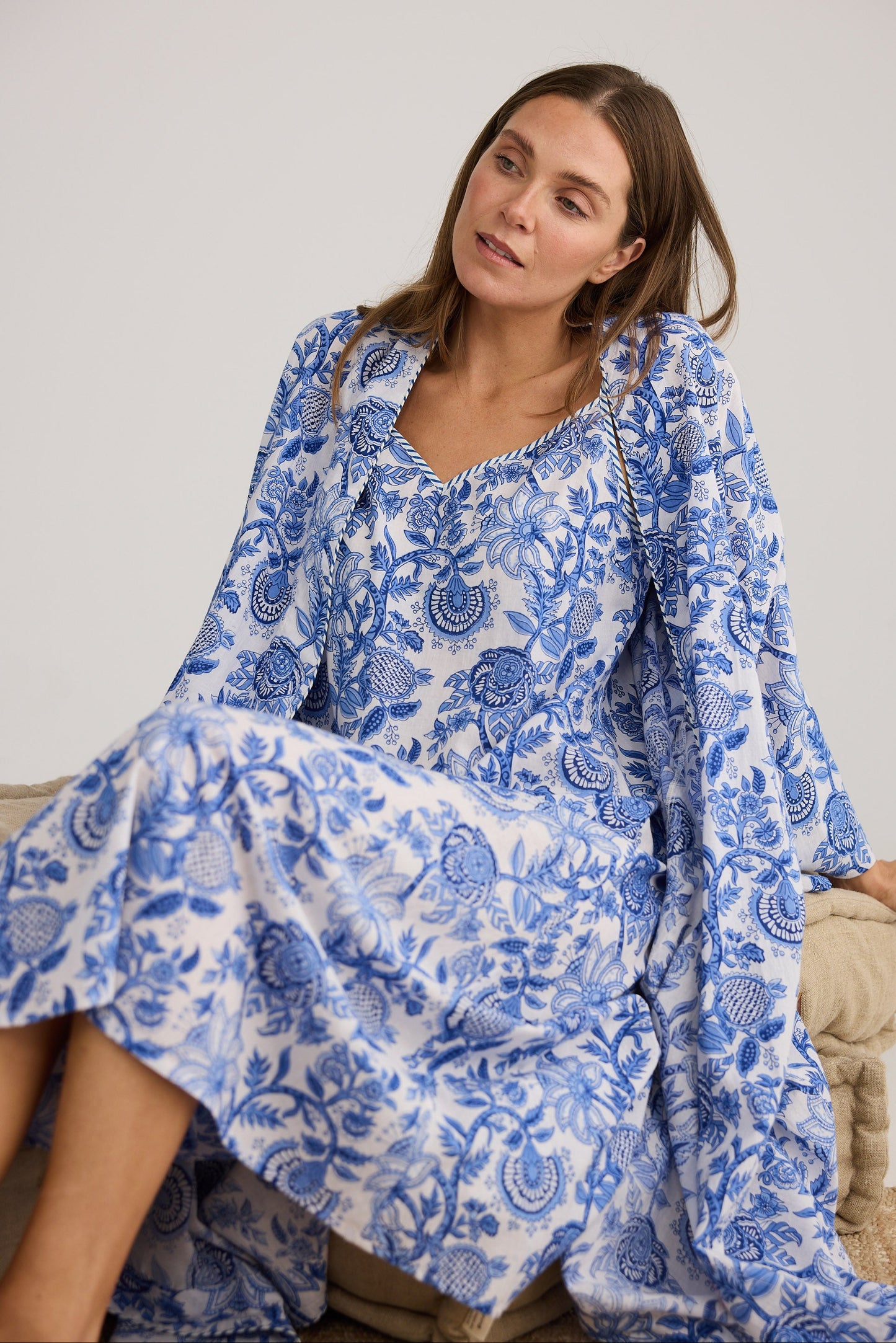 Woman wearing a blue floral dress and robe sitting on a white background