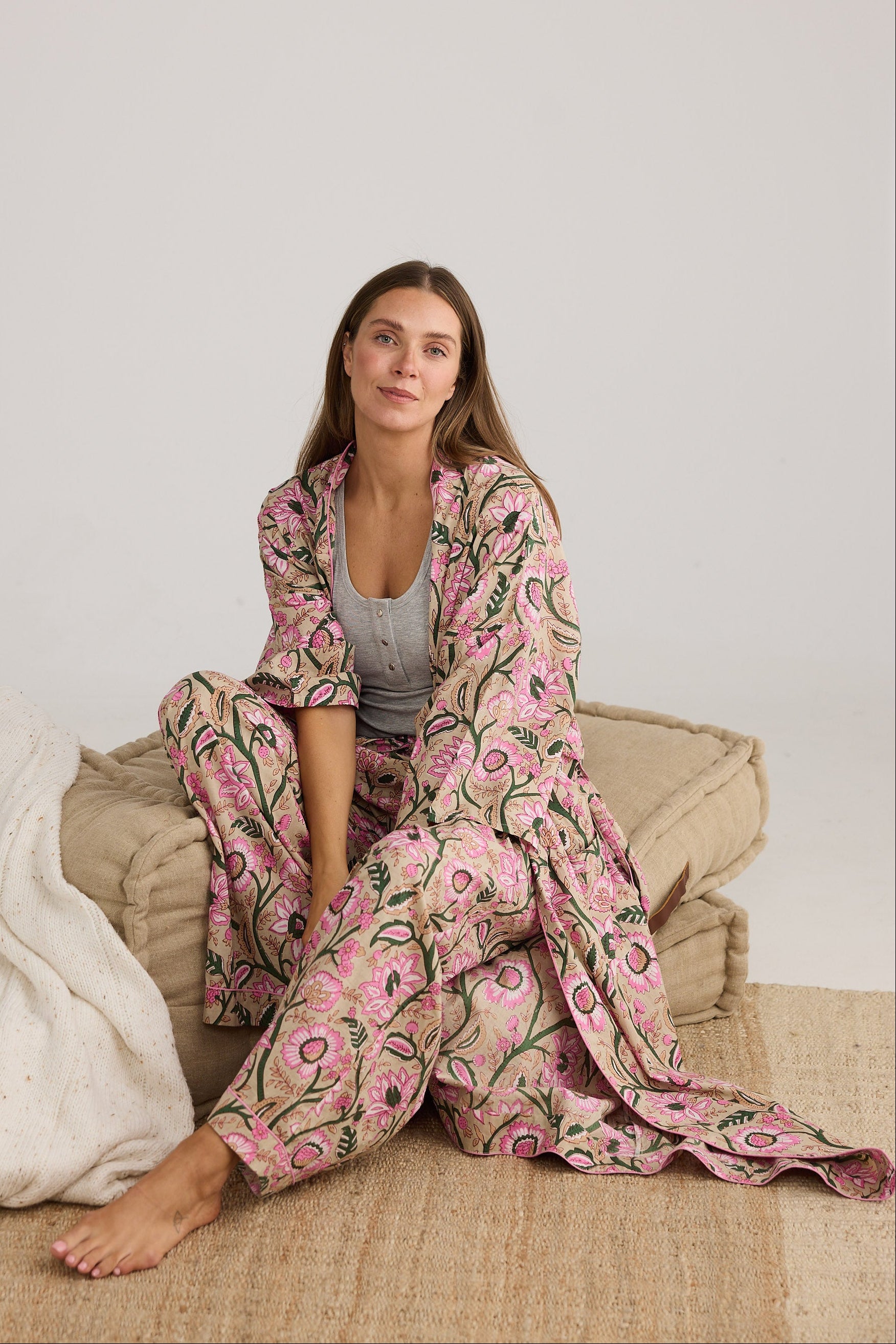 Woman wearing a pink floral pajama set sitting on a beige couch.