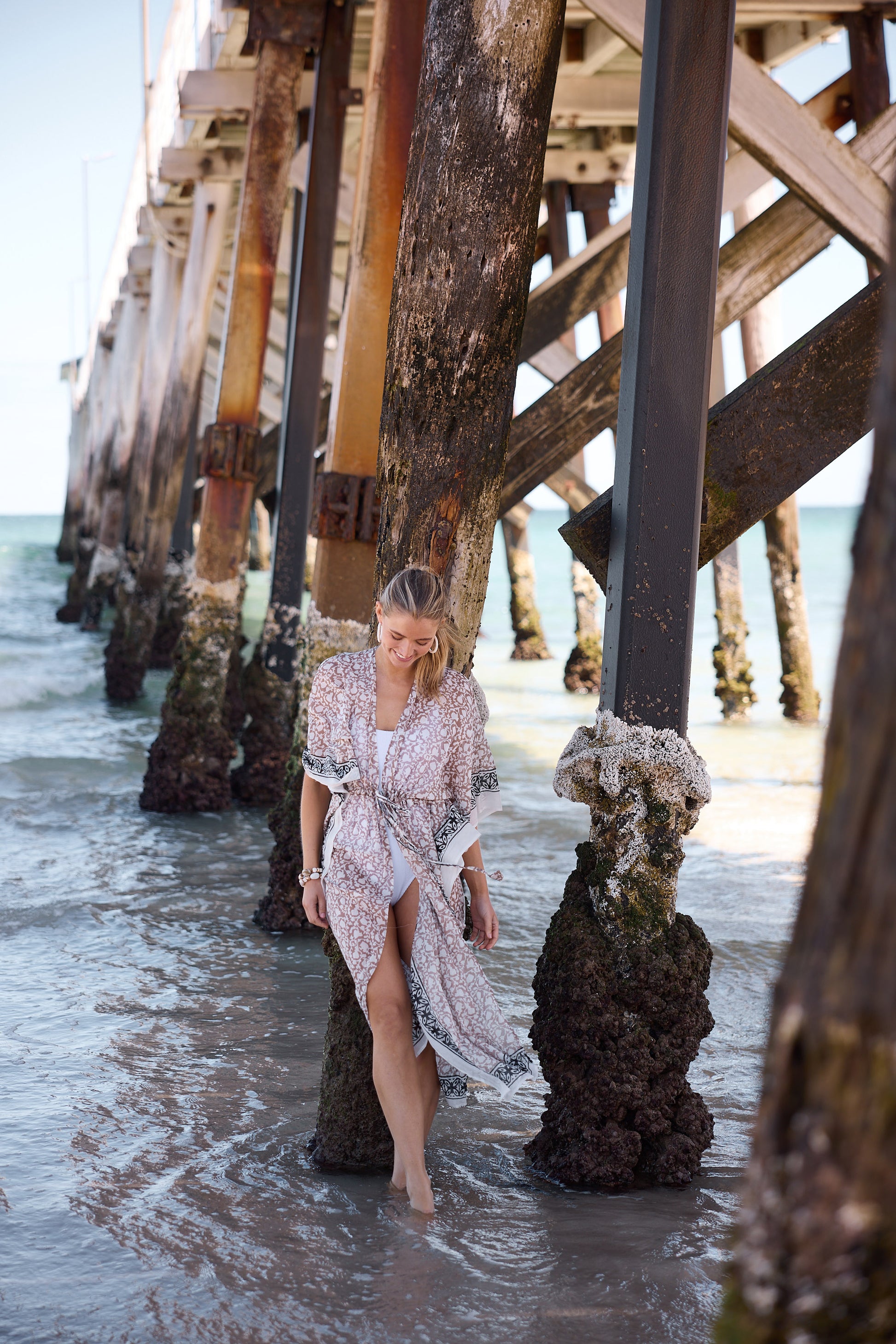 Woman in a dress standing on a beach near a wooden pier.