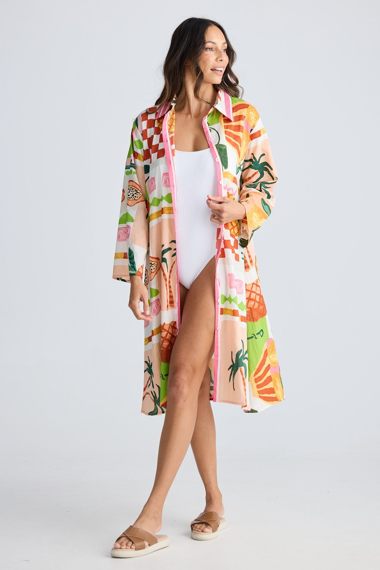 Woman wearing a colorful tropical print kimono over a white swimsuit on a light gray background