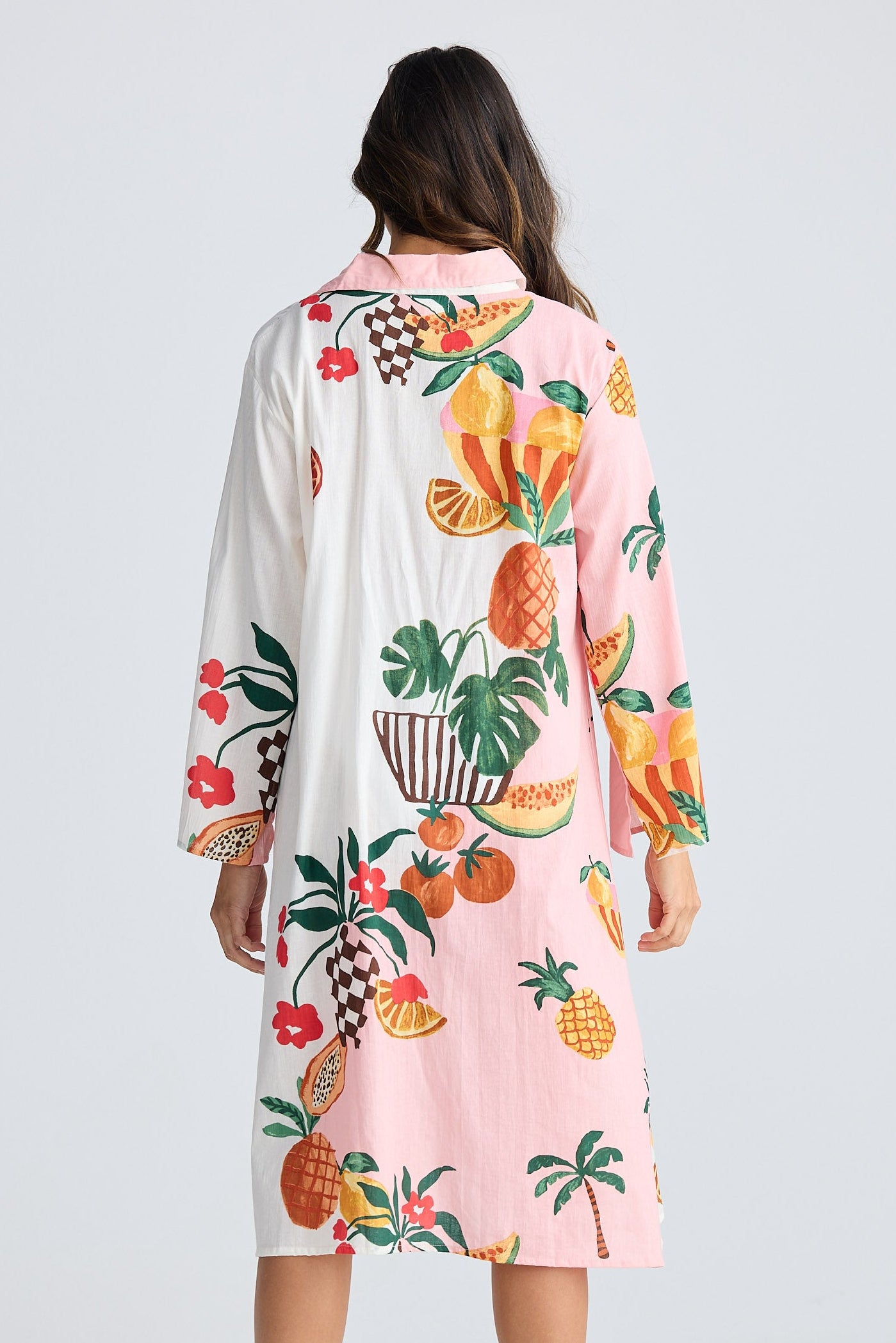 Woman wearing a long-sleeve dress with tropical fruit pattern on a white background