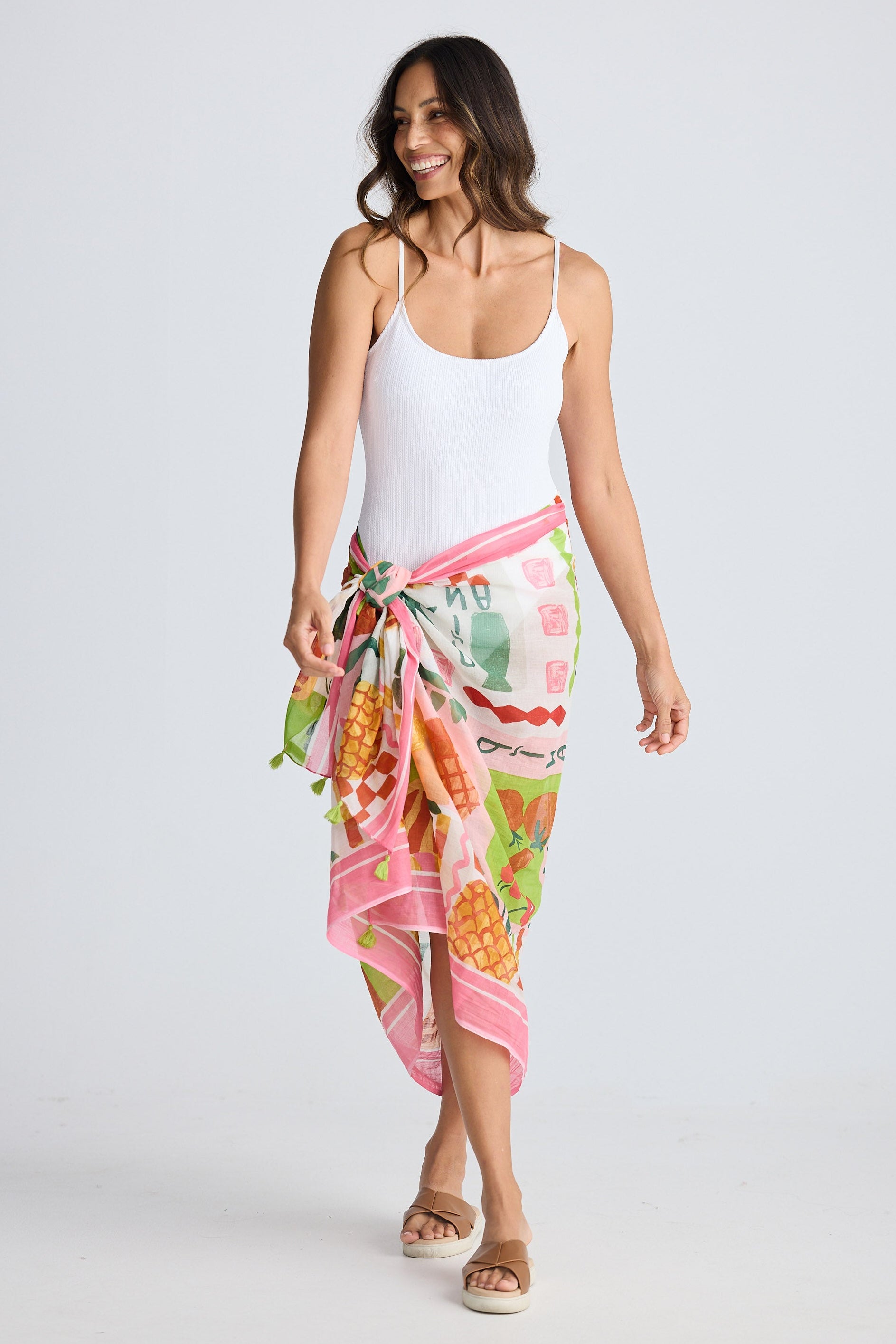 Woman wearing a colorful sarong over white bathers on a plain background