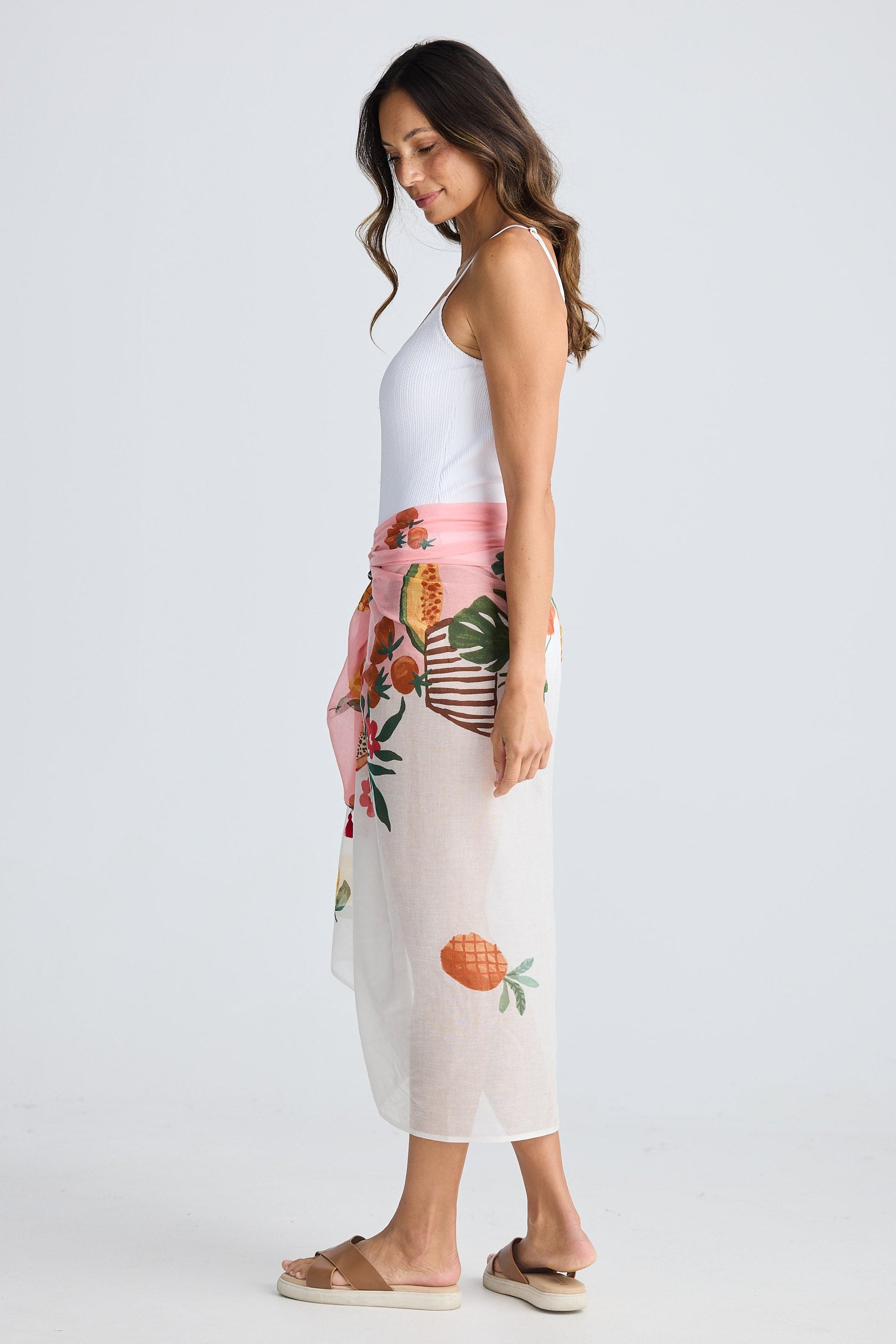 Woman wearing a white bathers and floral sarong with fruit design on a plain background