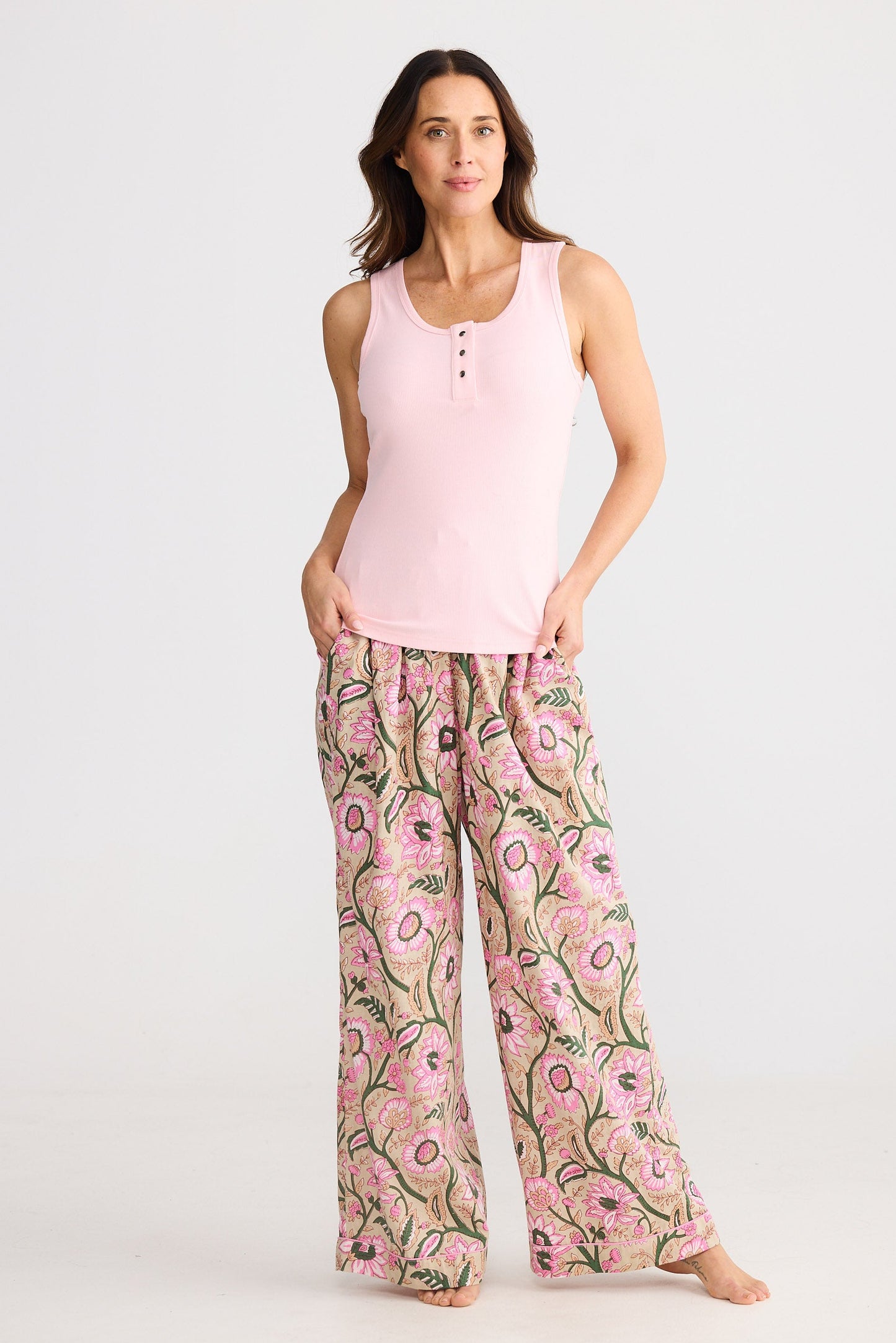Woman wearing a pink tank top and floral pants on a white background